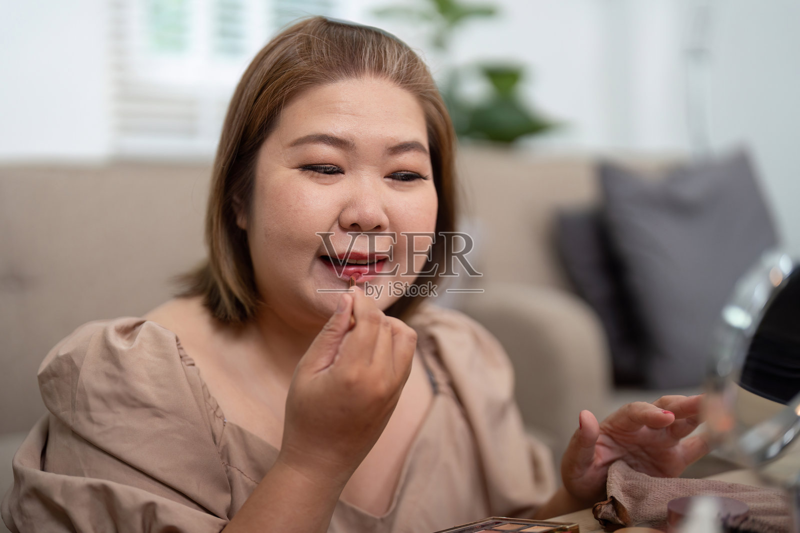 美容与唇部护理。一位女性在时尚的化妆角落微笑着涂口红。照片摄影图片