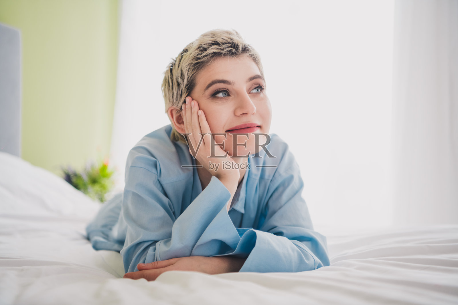 年轻女性穿着蓝色衬衫,在舒适的床上享受自然光线的放松时光照片摄影图片