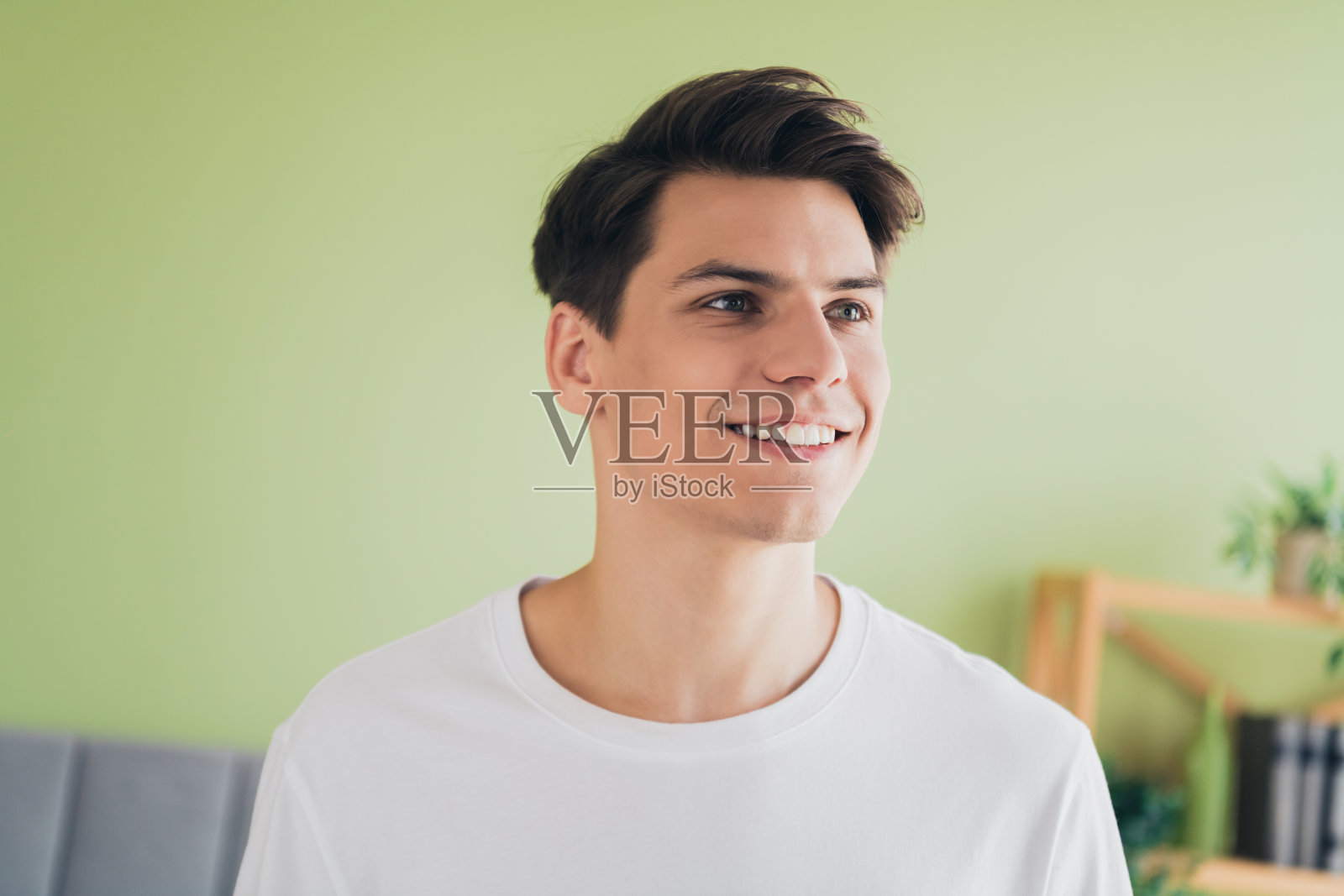 年轻快乐的男子穿着白色T恤,在温馨的家居环境中微笑,享受明亮的早晨。照片摄影图片