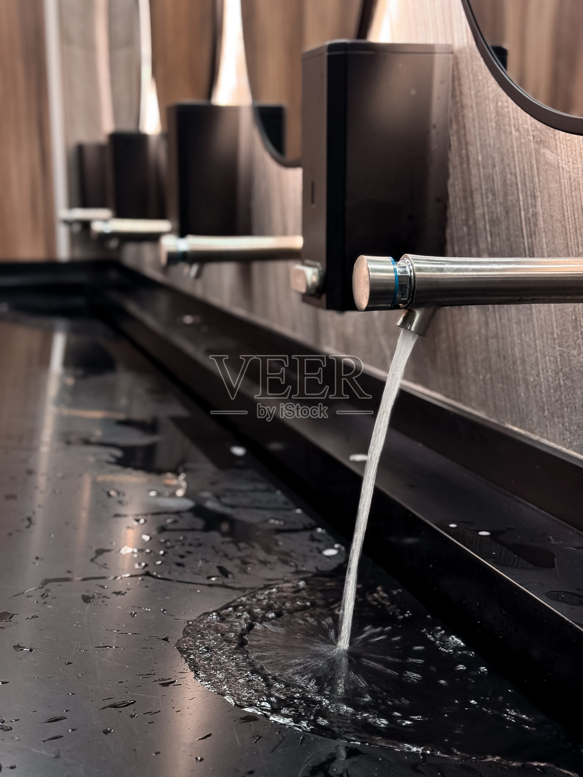 现代浴室洗手池,水龙头正在流出水,配有自动洗手液分配器照片摄影图片