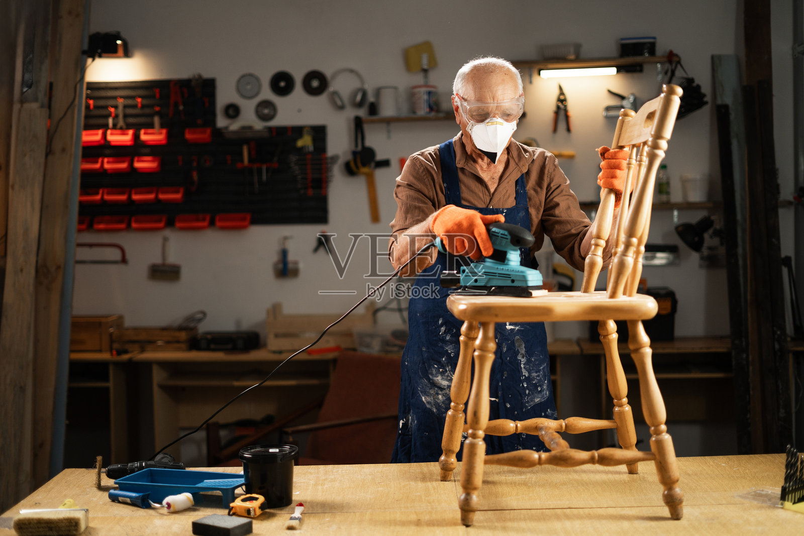 老年工匠正在用电动砂光机打磨木椅照片摄影图片