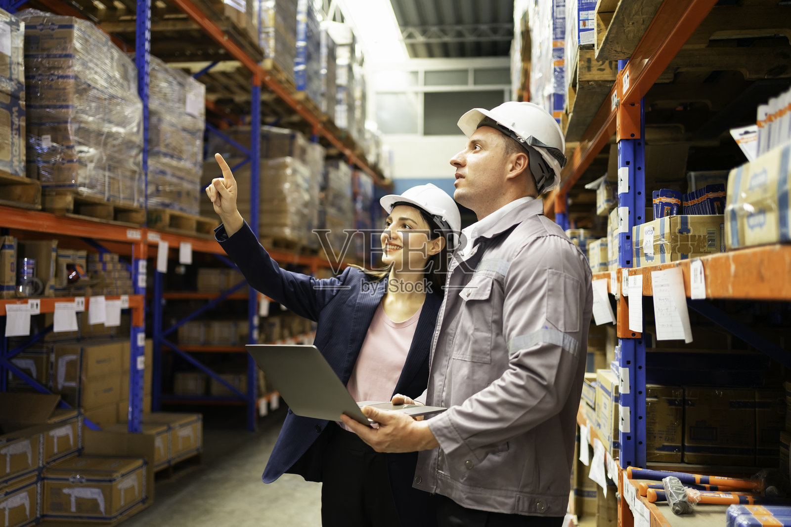 两位专业人士在仓库检查库存,讨论运营和物流,同时使用笔记本电脑进行数据分析。照片摄影图片