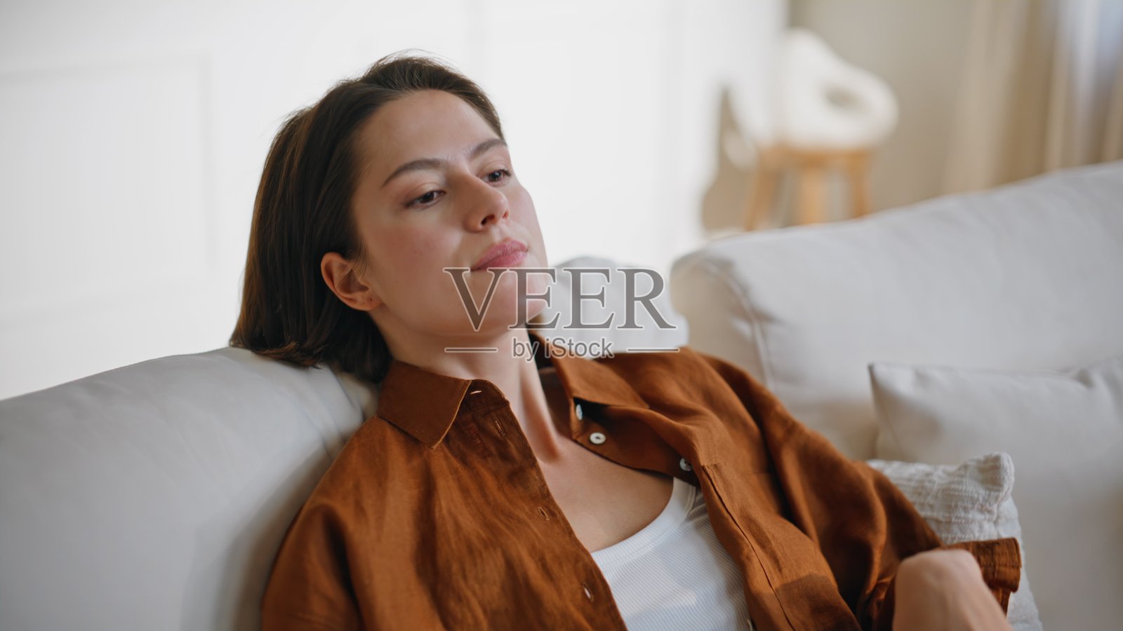 疲惫的女人靠在沙发上,特写肖像,棕发女子坐在沙发上。照片摄影图片