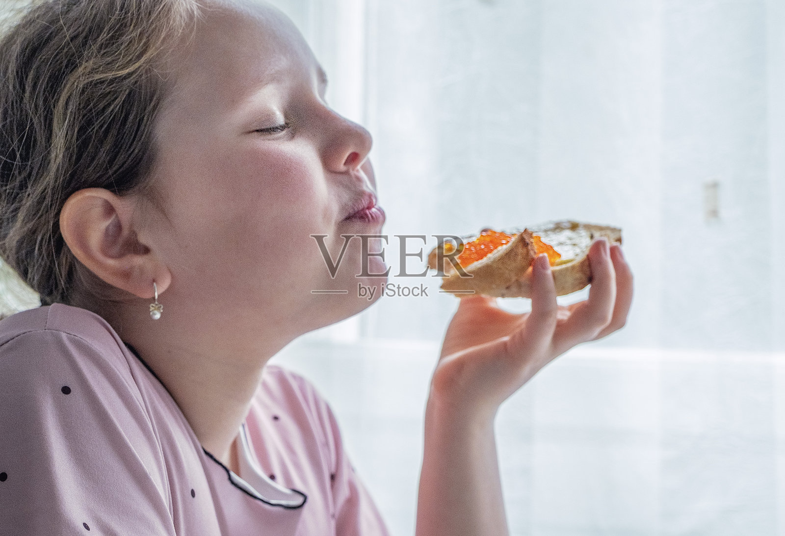 一个9岁的白人女孩正在享用一份涂有红鱼子酱的三明治,享受着美食。照片摄影图片