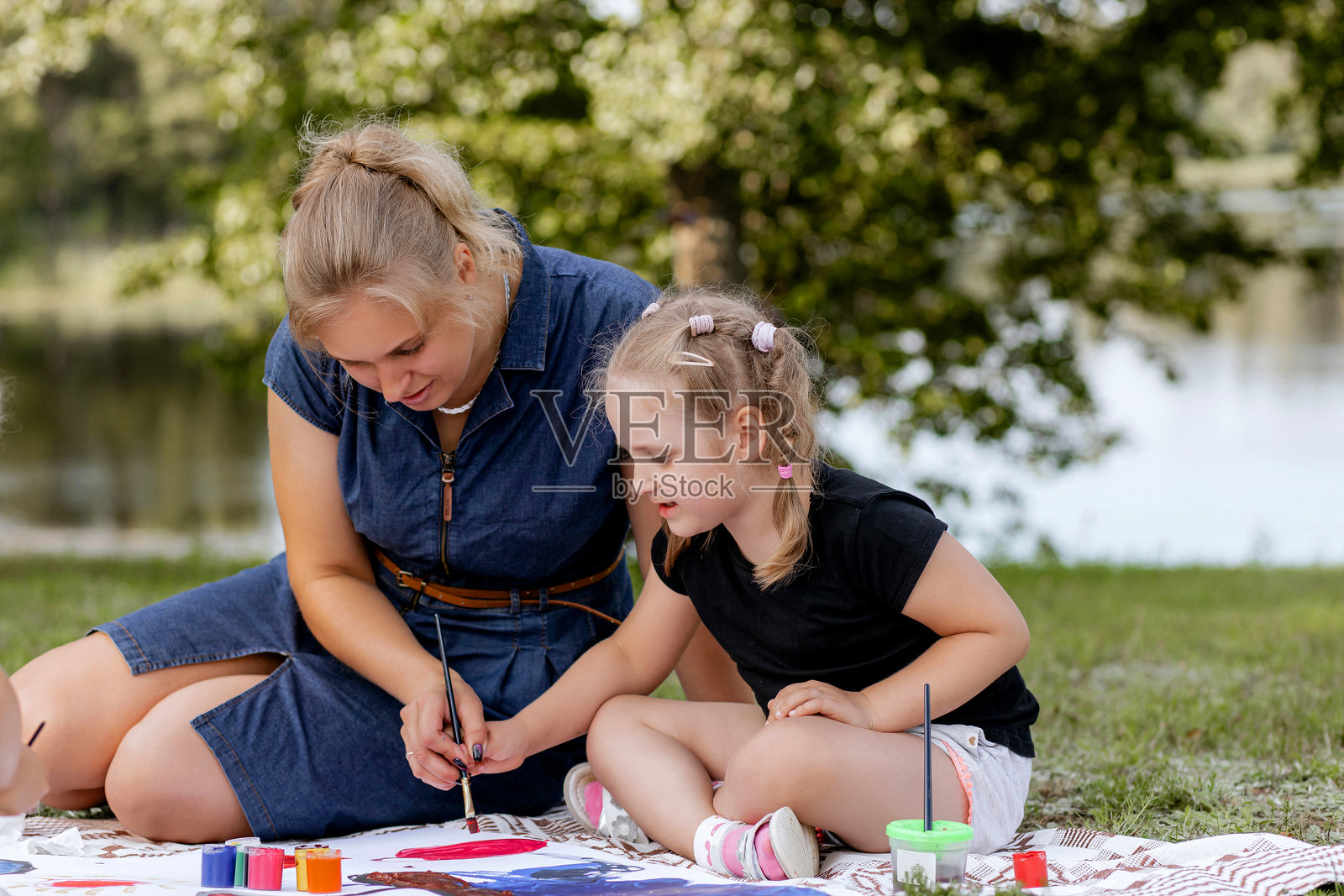 快乐的母亲和年轻的自闭症女儿在公园的野餐毯上画画——夏日里一起在大自然中进行创意家庭活动照片摄影图片