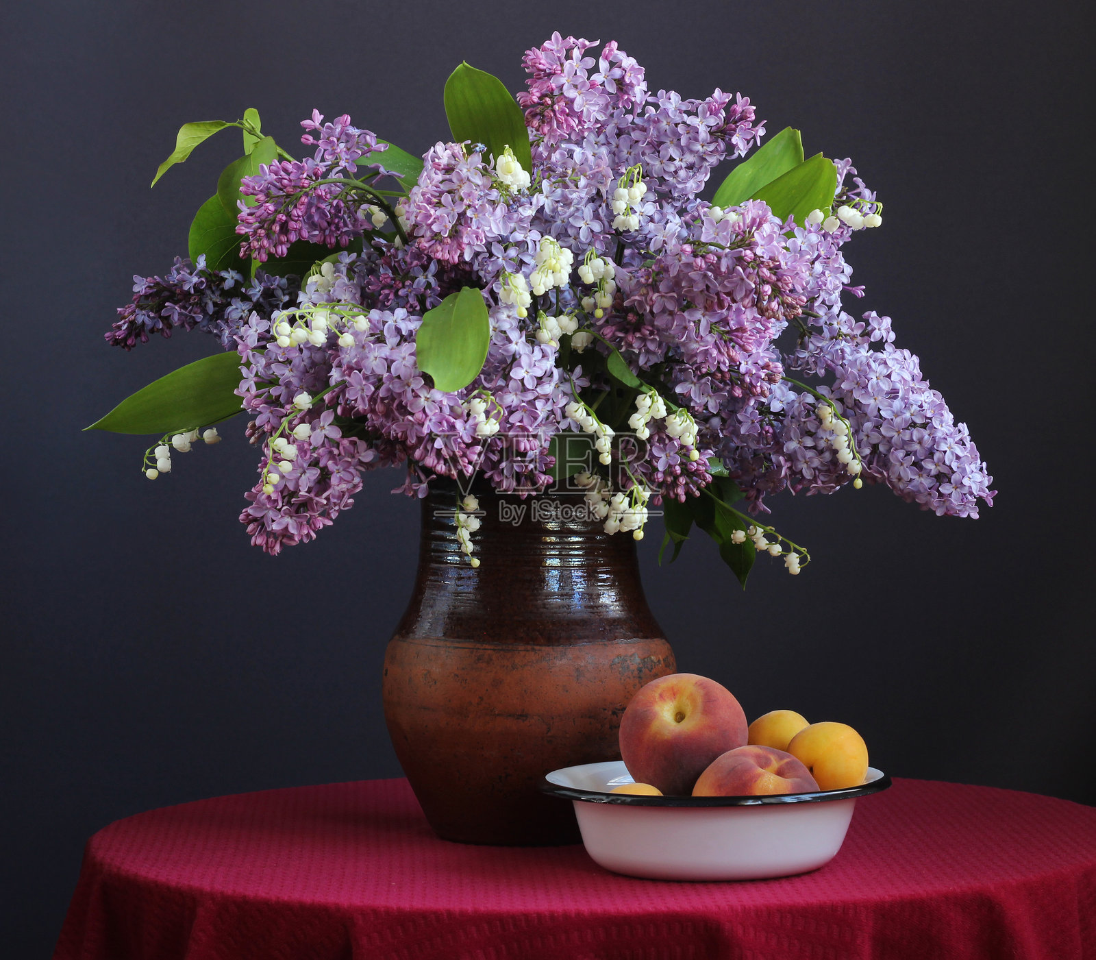 静物画:桌上铺着红色桌布的紫丁香、铃兰和桃子照片摄影图片