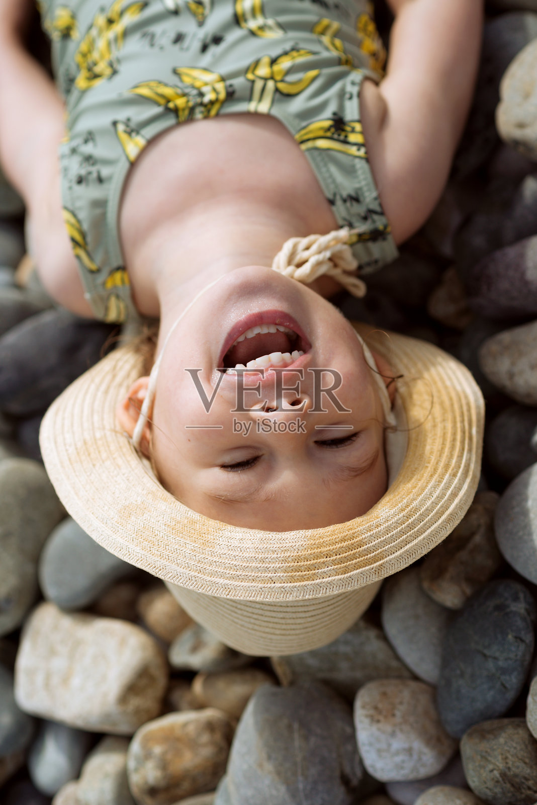 一个小女孩在岩石海滩上躺着,望着大海。照片摄影图片