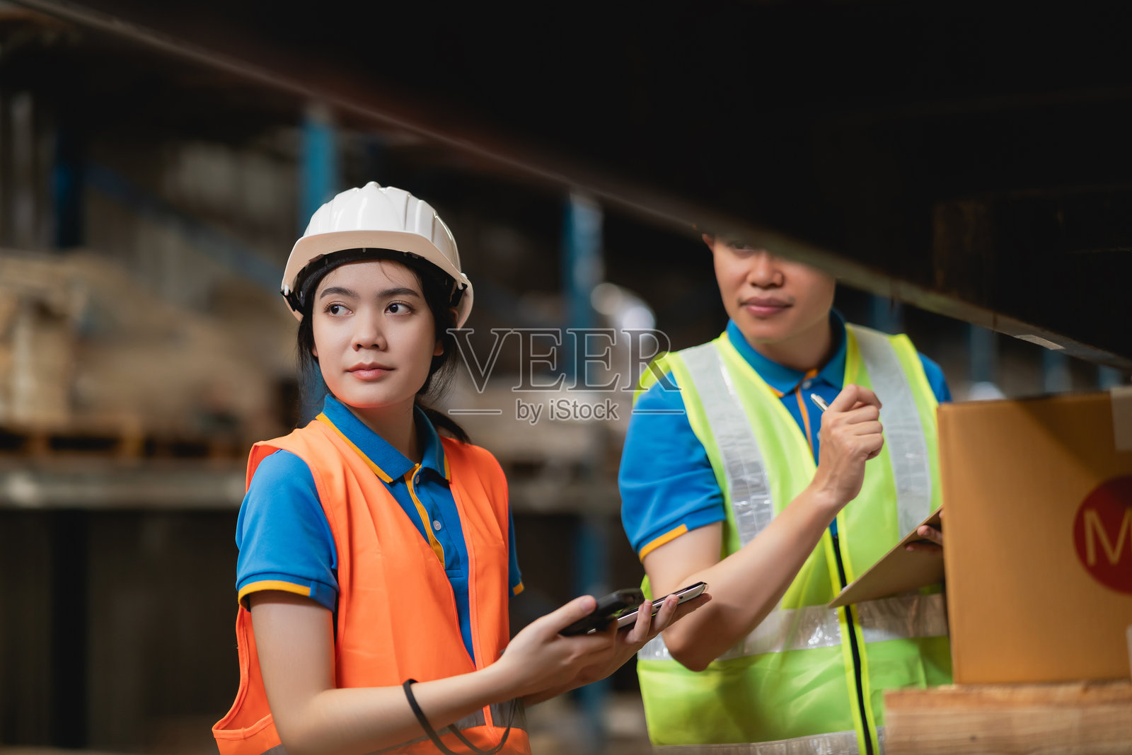 年轻女性仓库工人手持智能手机,与男性同事在大型配送中心检查库存照片摄影图片