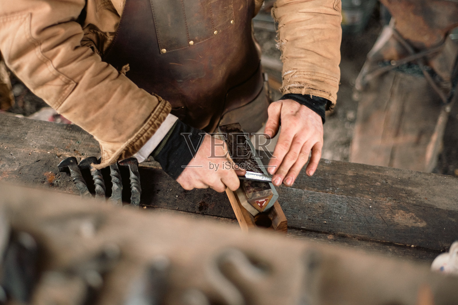 白人铁匠在密苏里州曼斯菲尔德的传统作坊中用磨刀石磨刀刃,工匠穿着皮围裙在铁坯上磨削钢工具的边缘。照片摄影图片