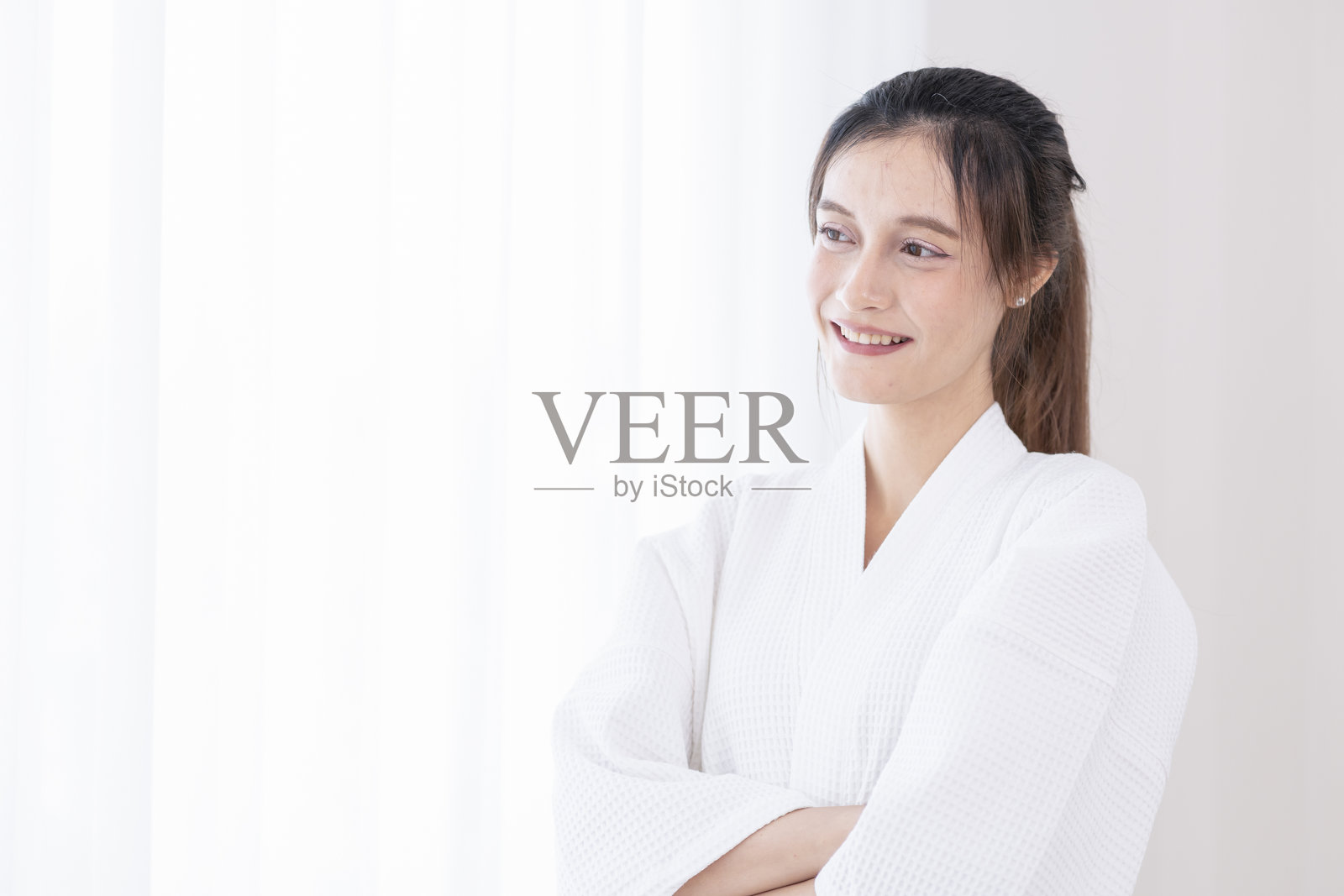 穿着浴袍的年轻漂亮女性在水疗室中站立,旁边留有文本空白。照片摄影图片