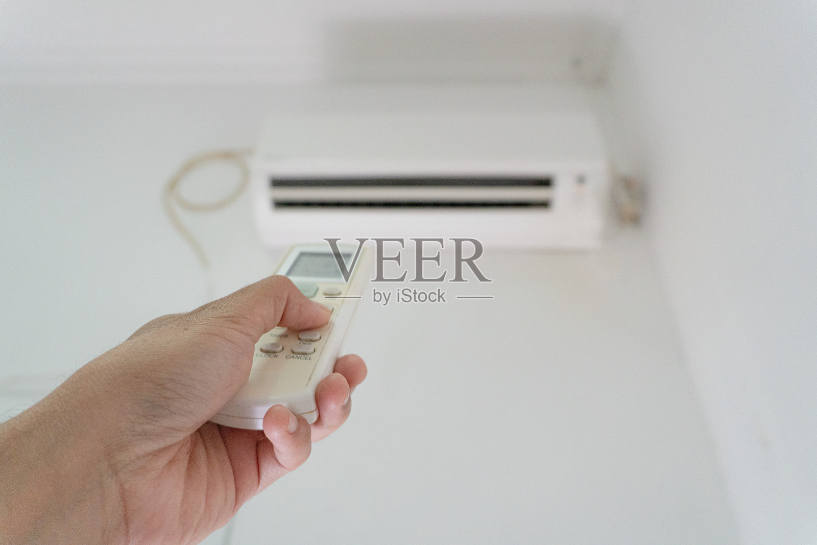 手握遥控器,指向墙上模糊的空调设备。调节温度或设置的概念。照片摄影图片