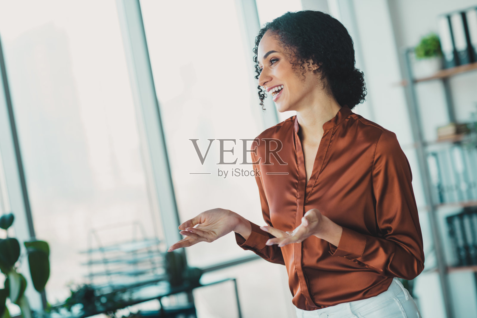自信的女商人穿着时尚的服装,在充满自然光的现代办公室中微笑着进行演示照片摄影图片