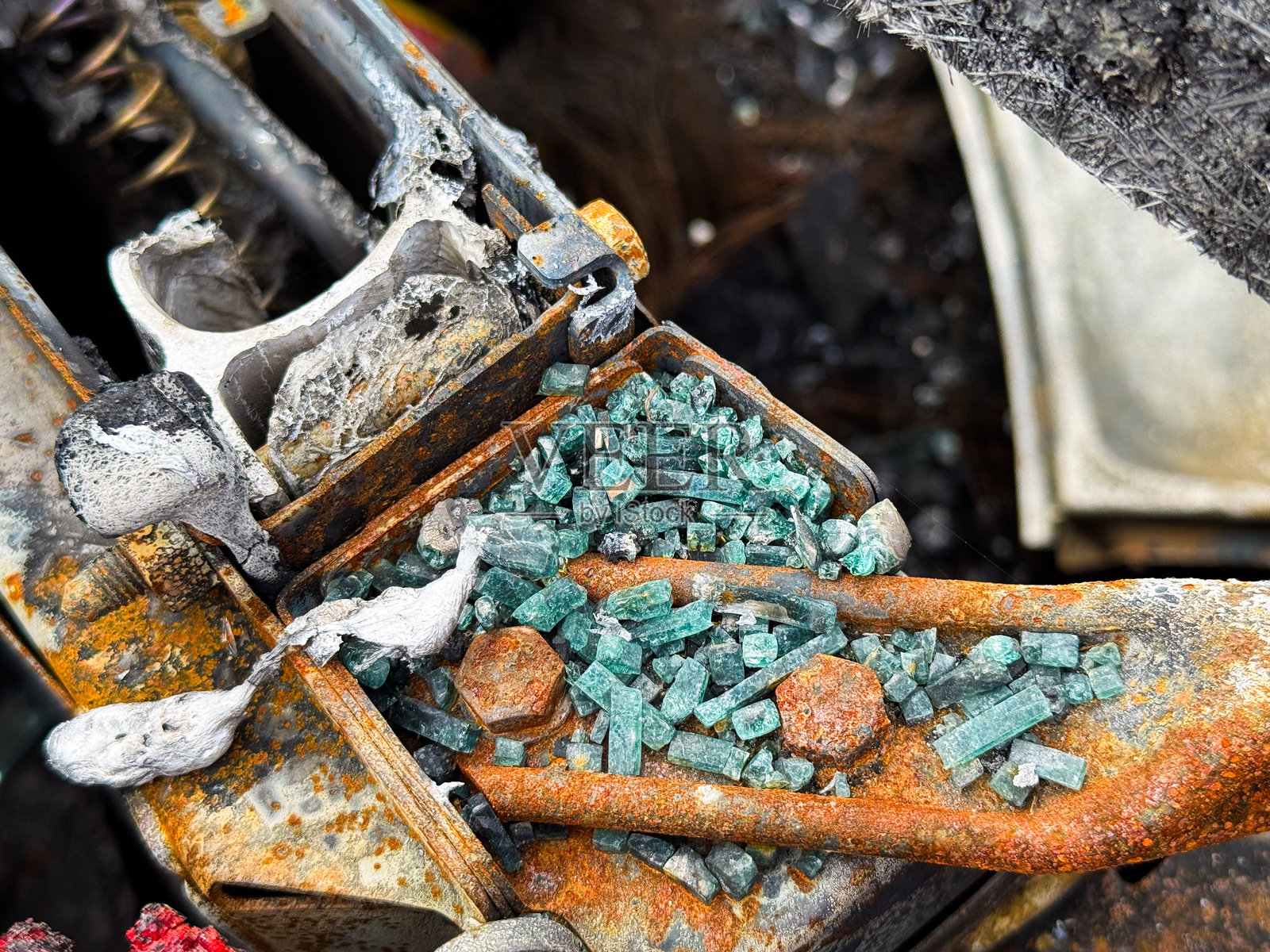烧焦和生锈的汽车座椅框架上散落着破碎的汽车安全玻璃特写,明显可见融化的部分和火灾损伤。照片摄影图片