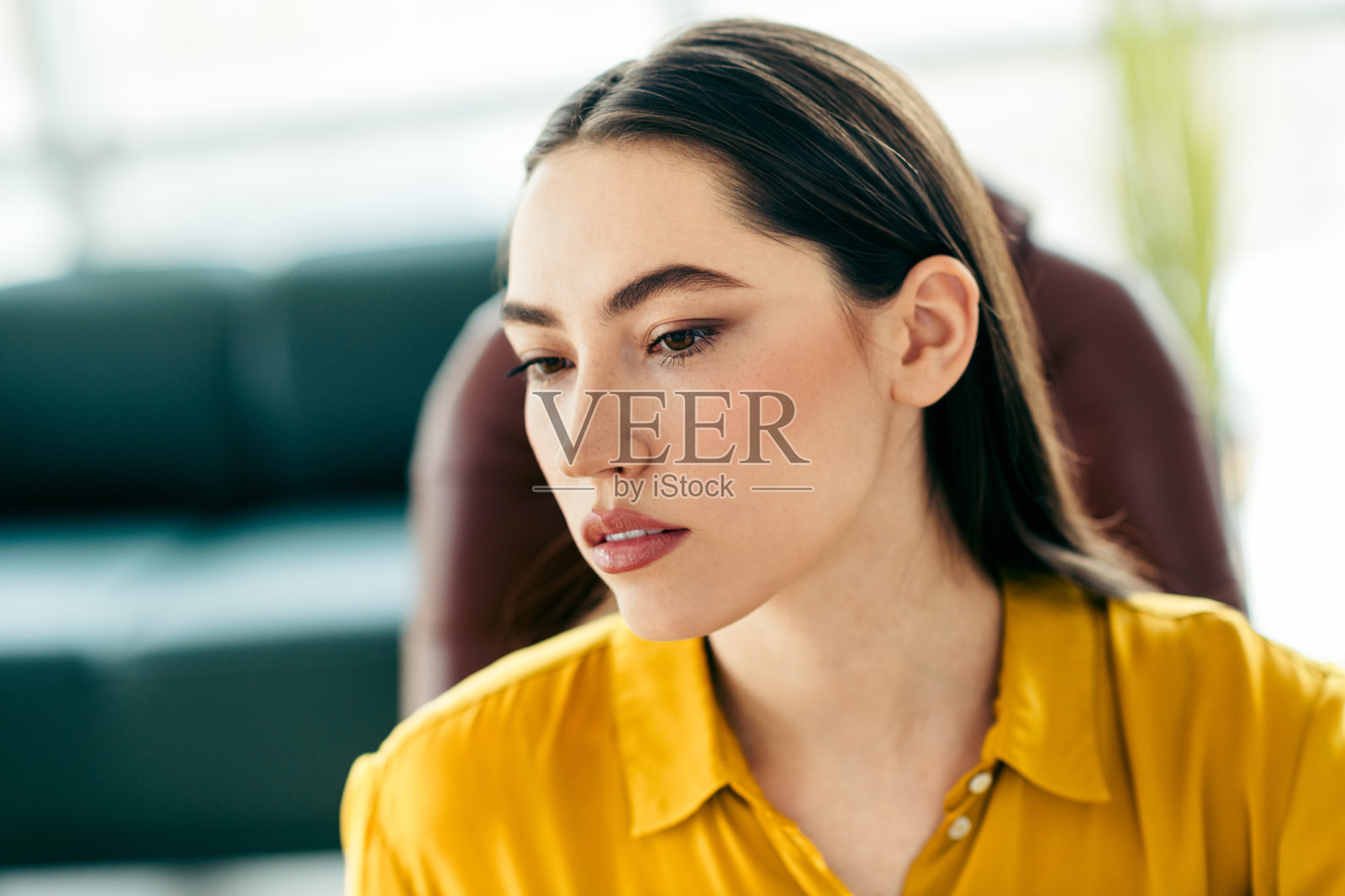 年轻职业女性穿着明亮的黄色衬衫,在现代办公室的自然光照下认真工作。照片摄影图片