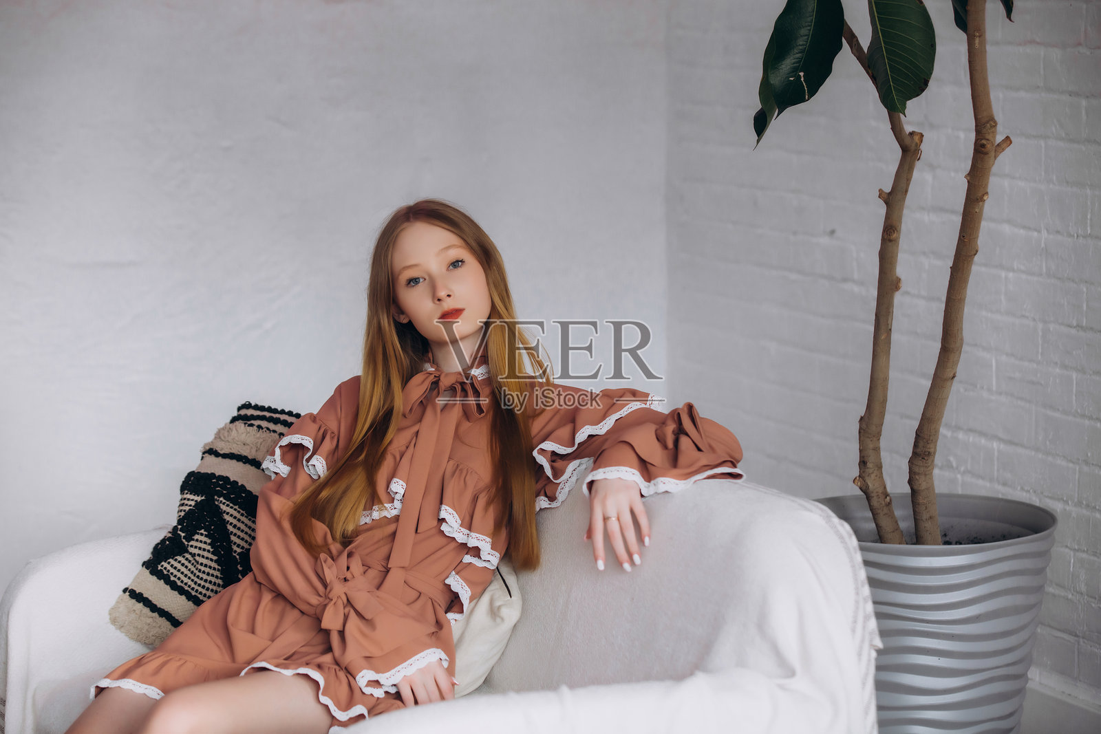 美丽的金发模特,年轻女孩,青少年,在室内沙发旁的蕾丝裙工作室中。照片摄影图片