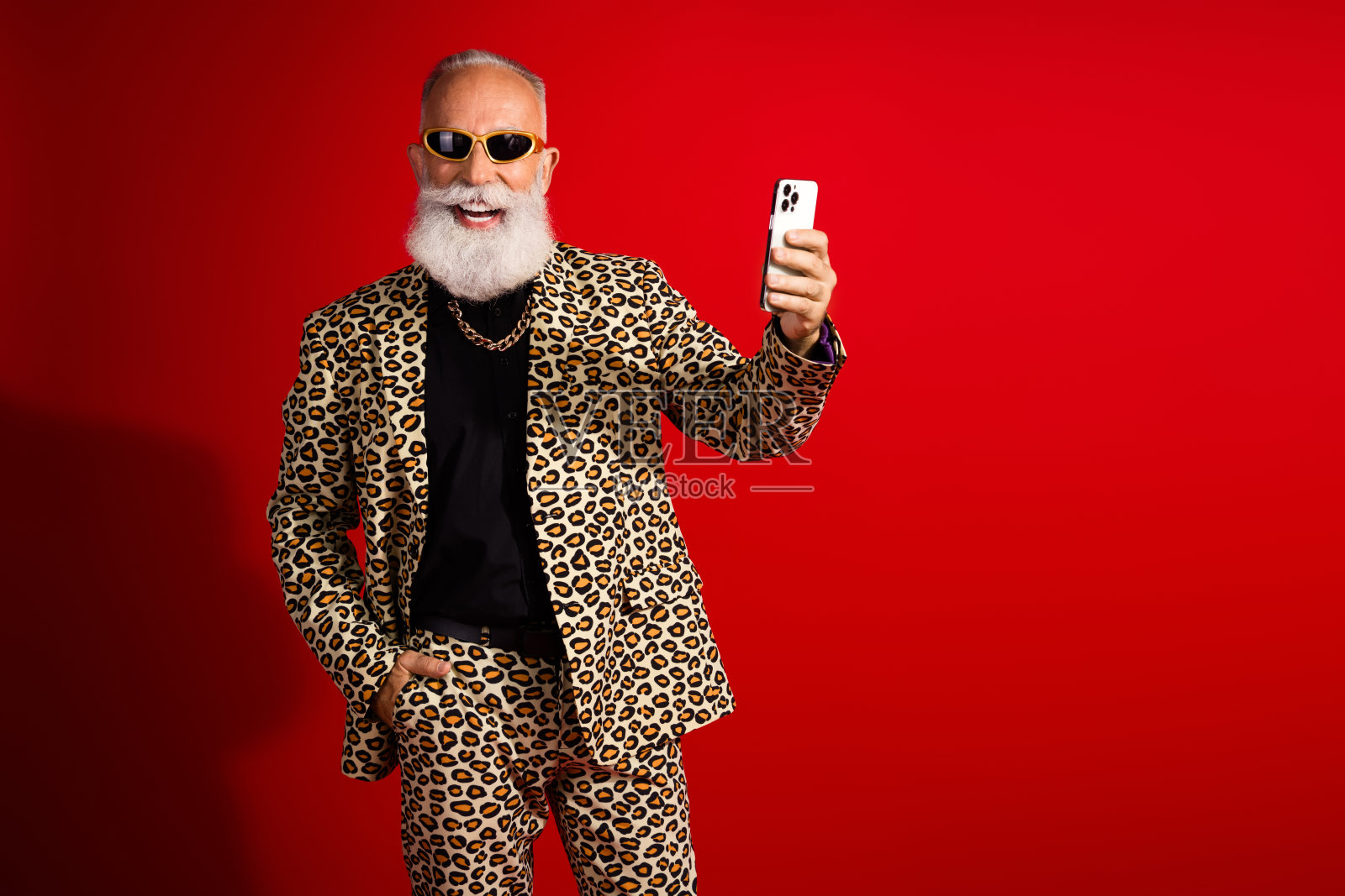 时尚的老年绅士穿着豹纹西装,手持手机,背景为红色。照片摄影图片