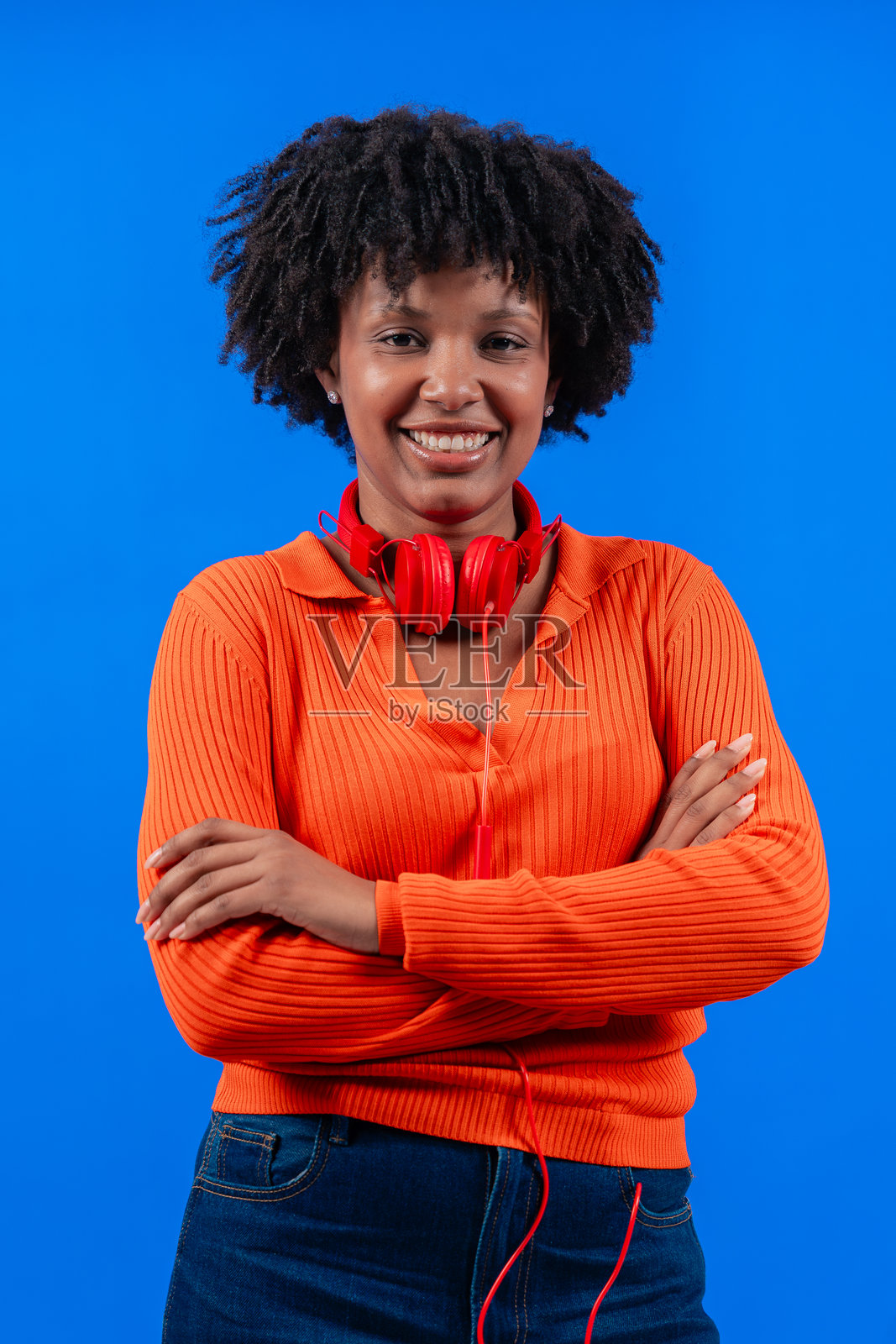 微笑的非裔美国女性戴着红色耳机,摆姿势于蓝色背景前照片摄影图片