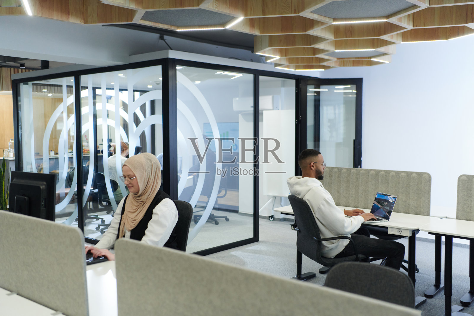 在现代办公室环境中,一位非裔美国商人与他的穆斯林同事(戴着头巾)进行合作讨论,共同处理各种商业任务和解决问题,展示了多样性、雄心和团队合作。照片摄影图片