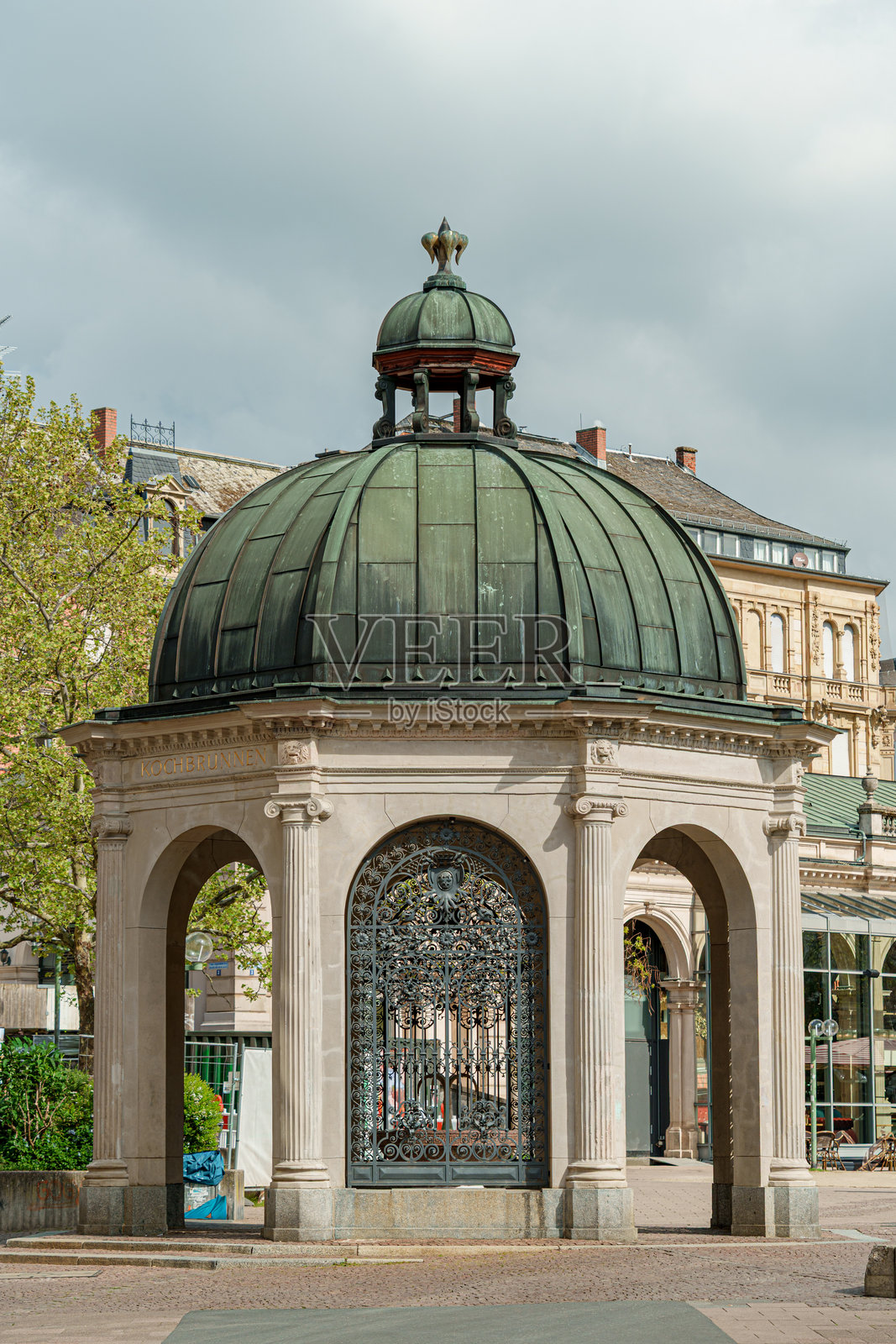 一个小巧的绿色圆顶烹饪喷泉亭,顶部镀金,坐落在kochbrunnenpavillon建筑前。照片摄影图片
