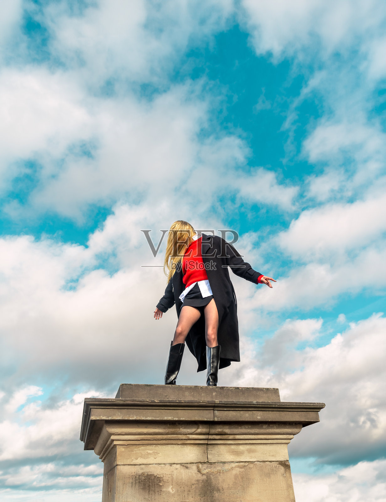 优雅的金发女人站在蓝天下的柱子上照片摄影图片