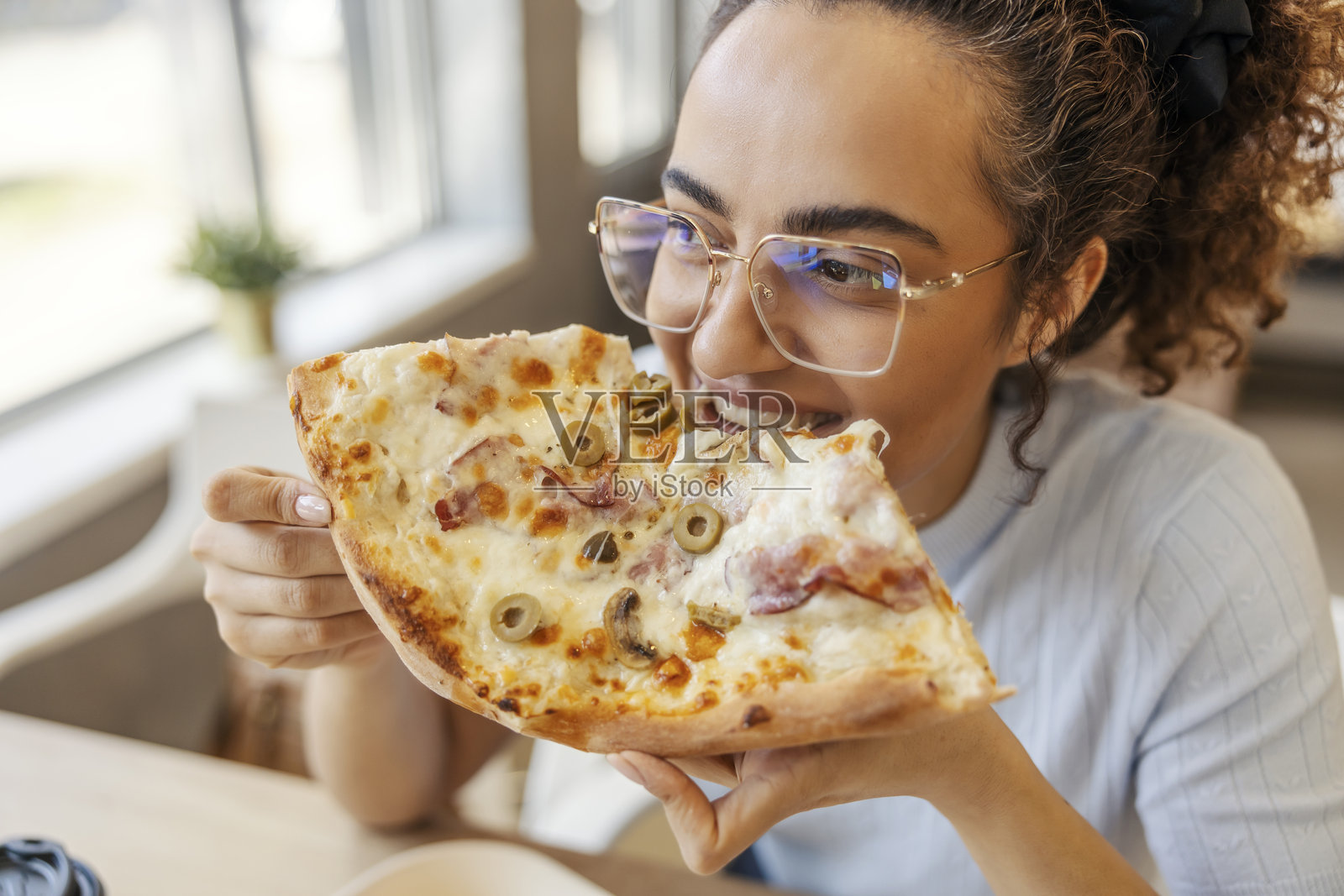 跨种族女孩在快餐店里咬比萨的肖像。照片摄影图片