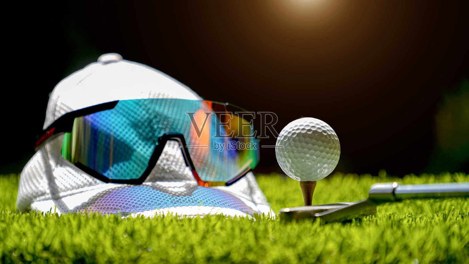 高尔夫球在球座上,白色高尔夫帽,太阳镜在高尔夫球场上照片摄影图片