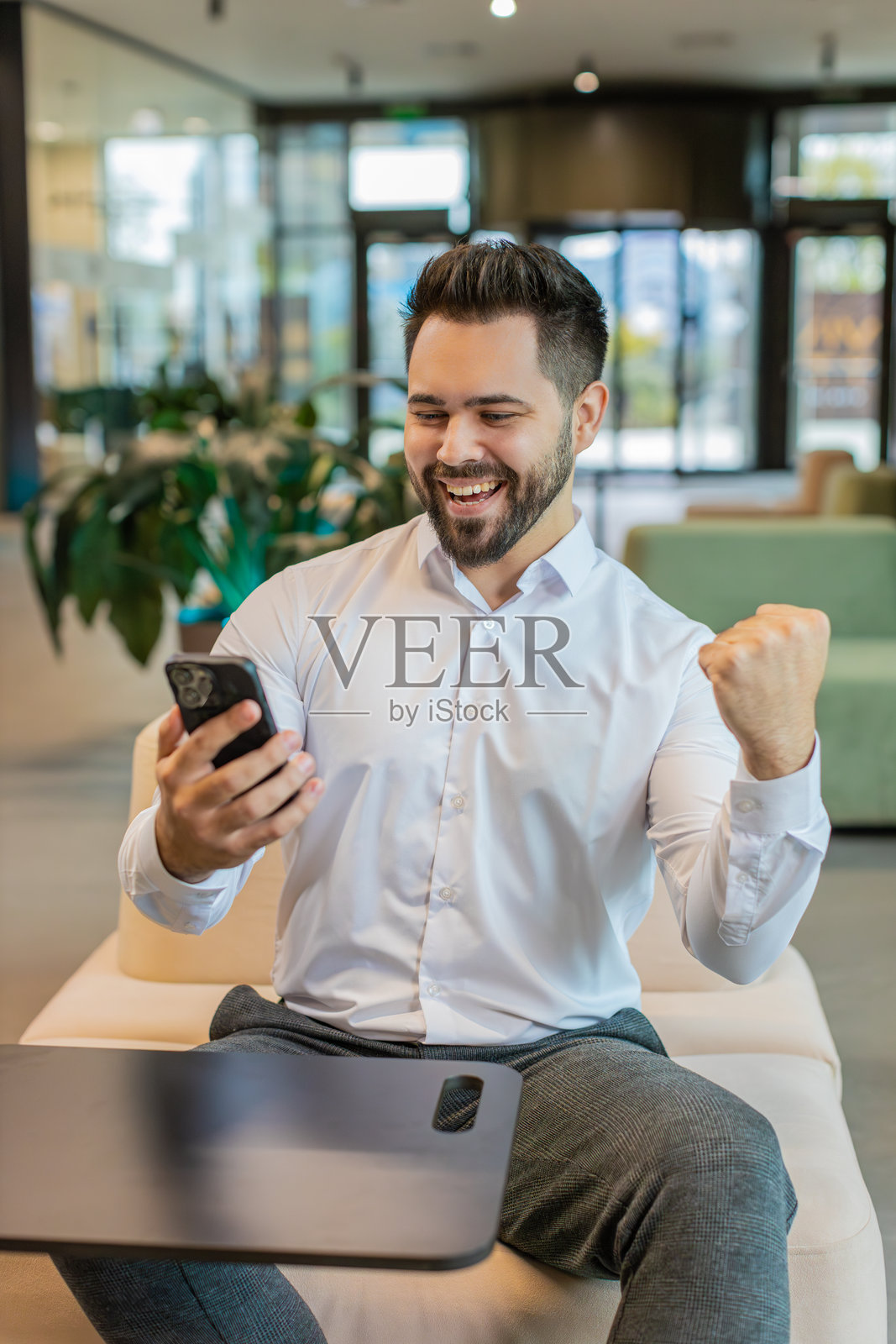 年轻的商人在办公室大厅里用智能手机惊讶于突然中奖的快乐时刻照片摄影图片