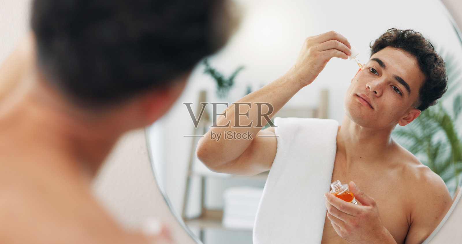 滴管,护肤或使用精华液的男性,旨在提升美容光泽或面部光彩,场景为家中、浴室或公寓。面部、脸颊或使用精油保湿剂的人,旨在获得胶原蛋白、维生素C的美容效果或益处。照片摄影图片