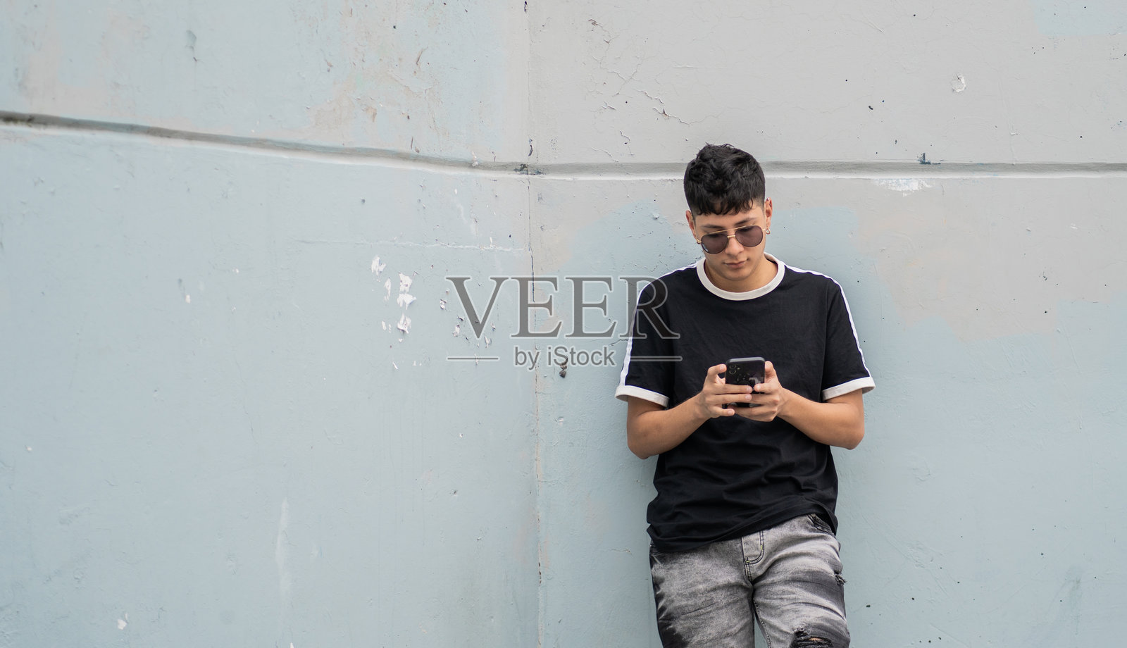 城市年轻人靠在墙上使用手机 - 股票照片。照片摄影图片