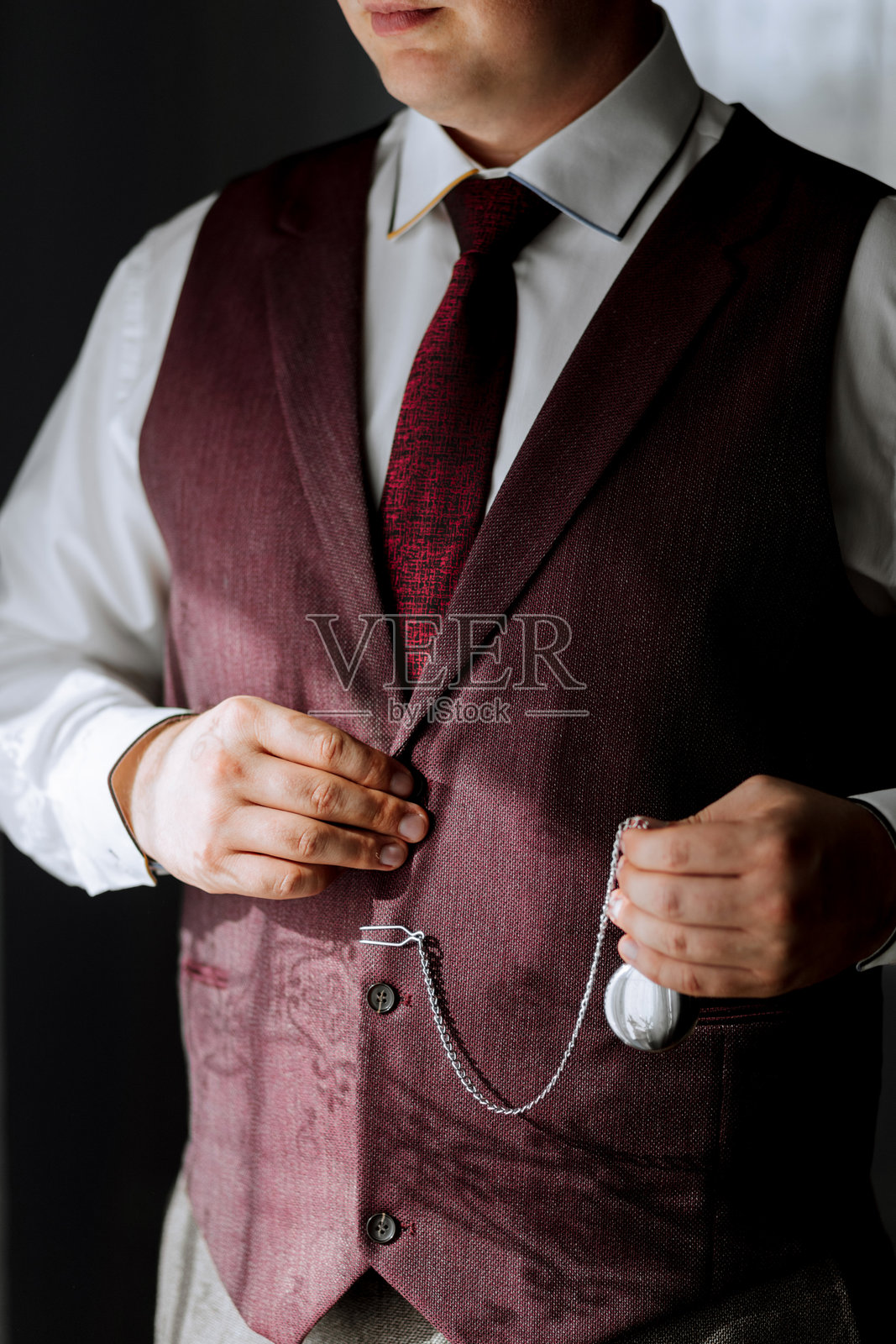 一名穿着红色背心和白色衬衫的男子正在整理他的领带照片摄影图片