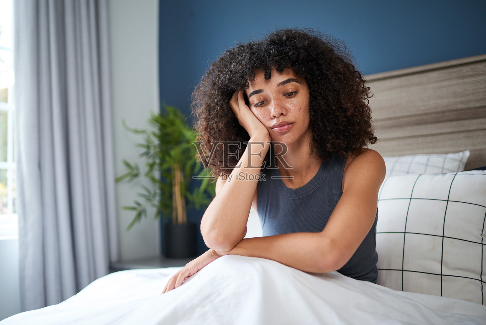 年轻女性坐在卧室的床上,若有所思,沐浴在自然光中照片摄影图片