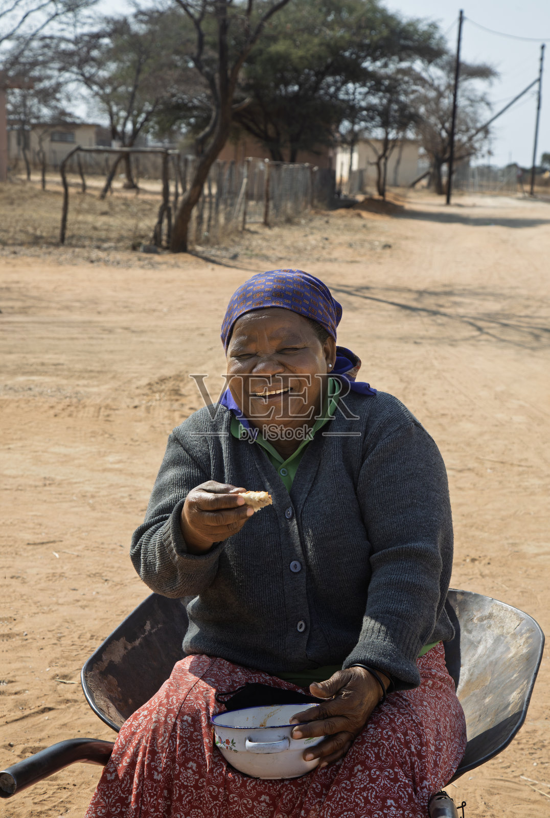 村庄里一位笑容满面的非洲老妇人坐在手推车上,向大家提供面包和炖菜。照片摄影图片
