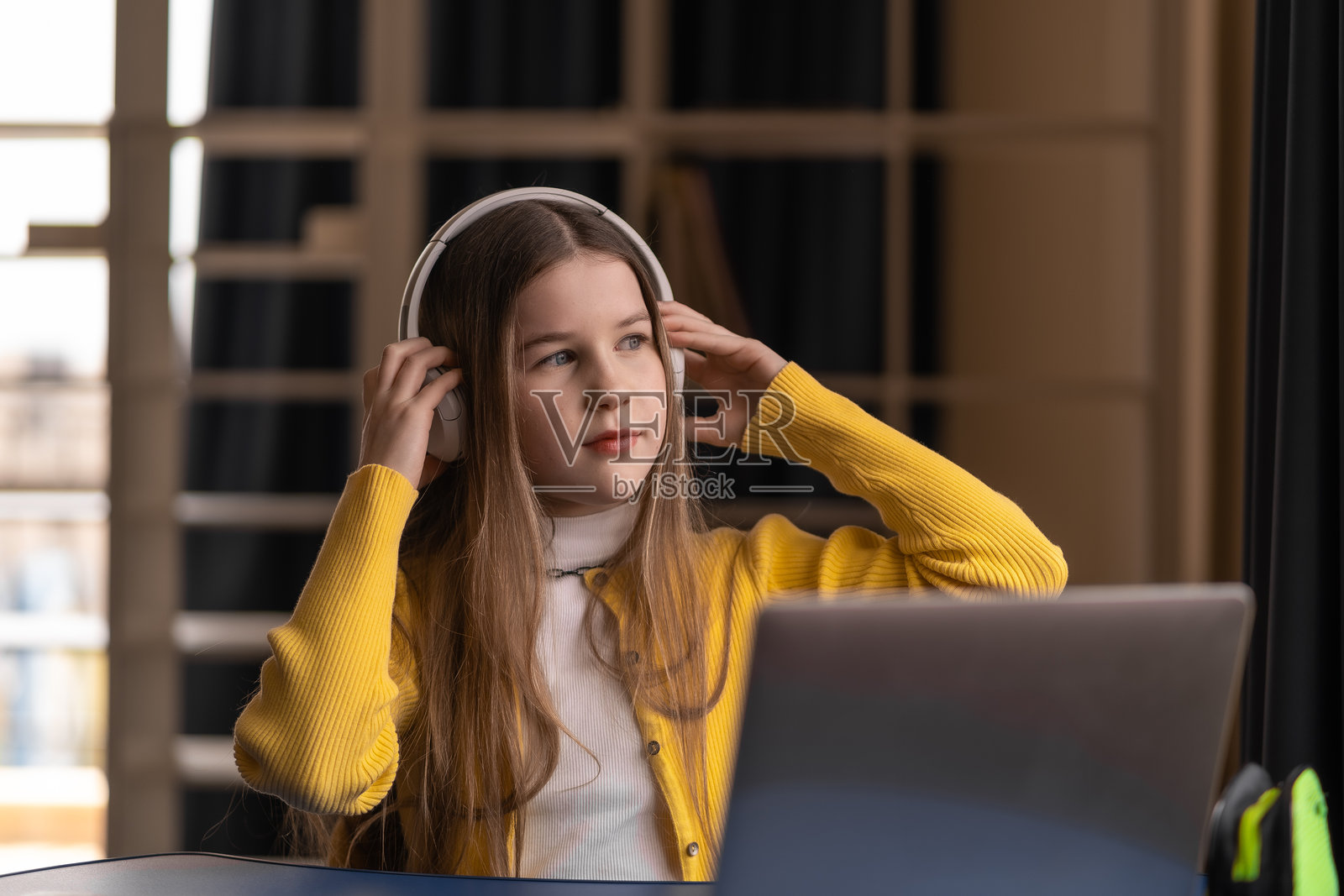 戴着耳机的女学生在宁静的数字环境中学习,使用笔记本电脑和笔记本,展示了混合学习的自信、自我组织能力和现代数字教育。照片摄影图片