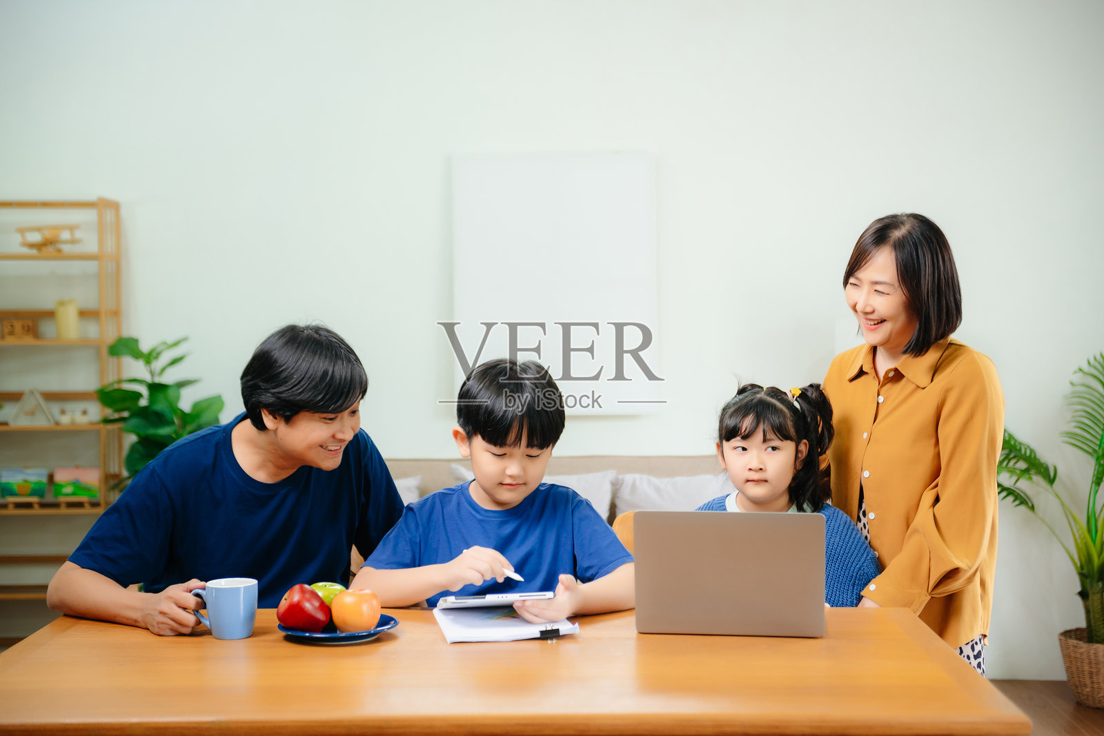 亚洲小男孩在家学习,使用电脑和平板做作业,母亲在旁帮助、教导和鼓励他。照片摄影图片