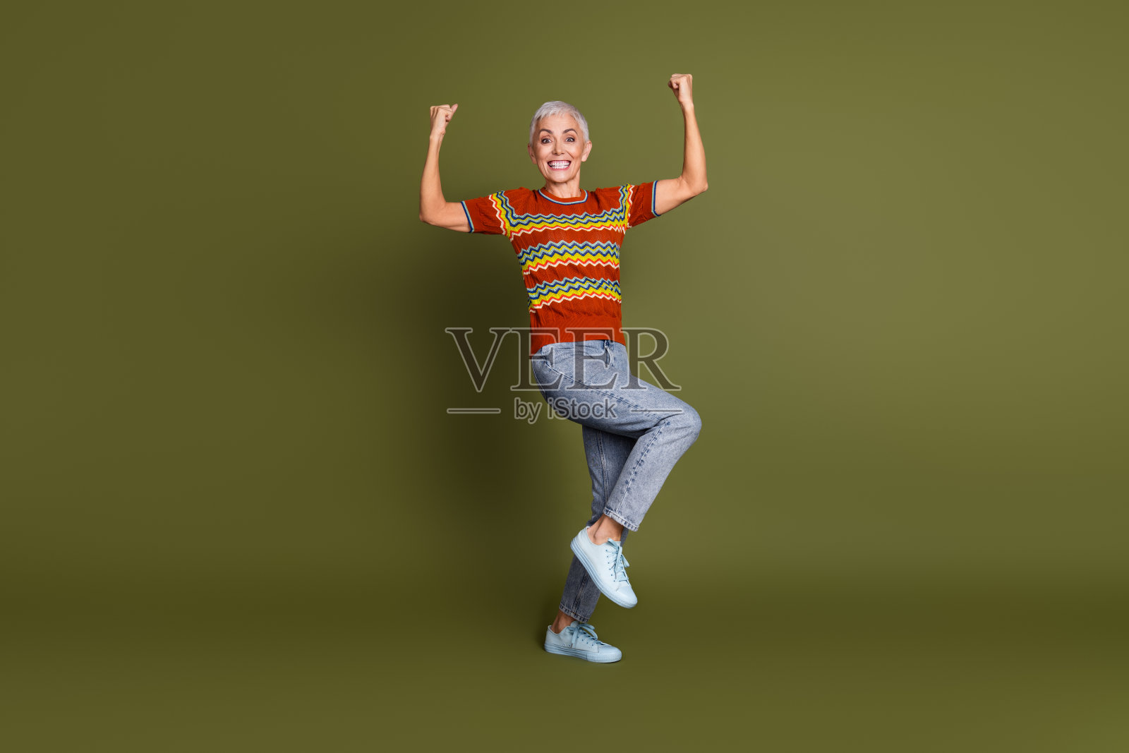 穿着色彩斑斓服装的老年女性在绿色背景下快乐地跳舞,展现出活力与幸福。照片摄影图片