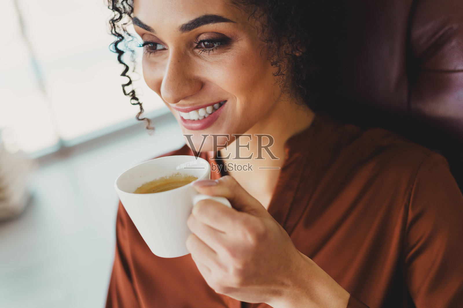 年轻女商人在明亮的工作空间中享受咖啡休息,穿着时尚的服装,展现出自然自信的气质照片摄影图片