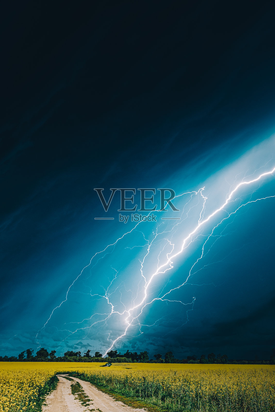 戏剧性的雨天天空,地平线上有雨云,映衬着乡村风景和油菜花田。乡间小路。农业与天气预报概念。照片摄影图片