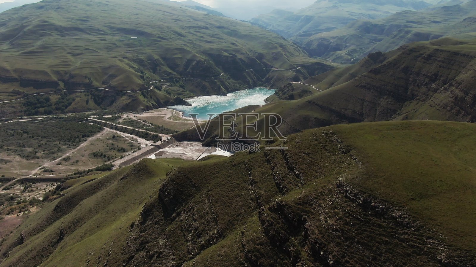 一片清澈的山湖,形状不规则,位于绿色山丘之间。照片摄影图片