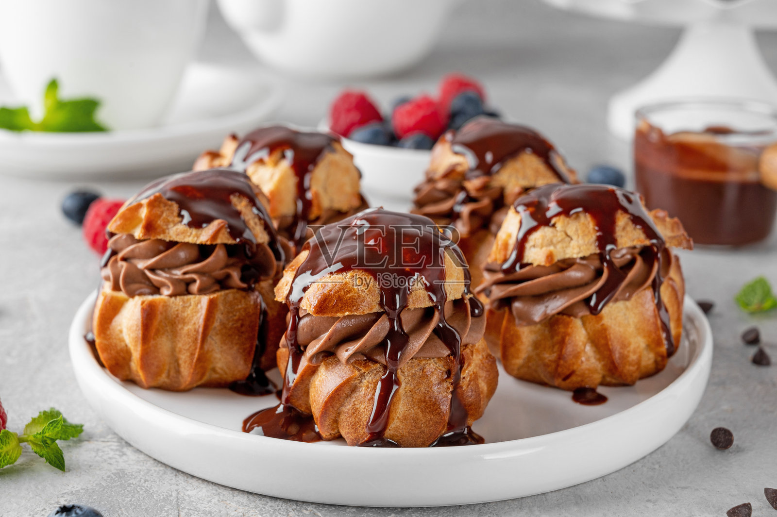 盘子上摆放着巧克力奶油、鲜莓和巧克力糖霜的泡芙,背景为灰色混凝土。这是一道美味的法式甜点。照片摄影图片