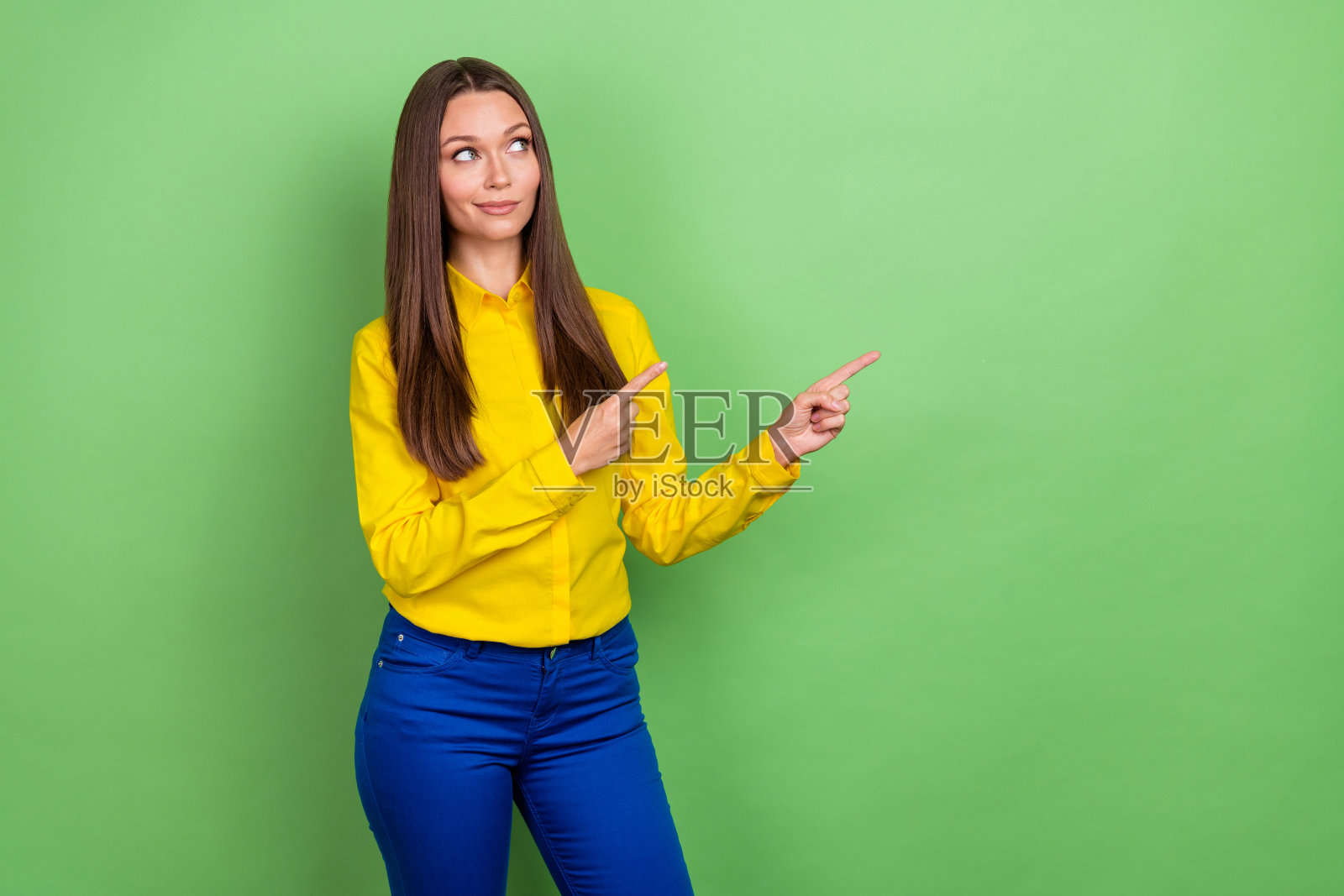 年轻的棕色发型女士穿着衬衫和裤子,站在绿色背景前,展现促销形象。照片摄影图片