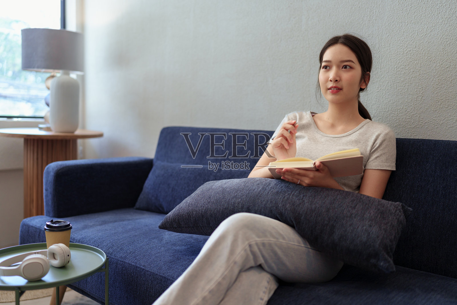 平静的年轻女性坐在沙发上,在温馨的家居环境中写日记,享受宁静的时光。照片摄影图片