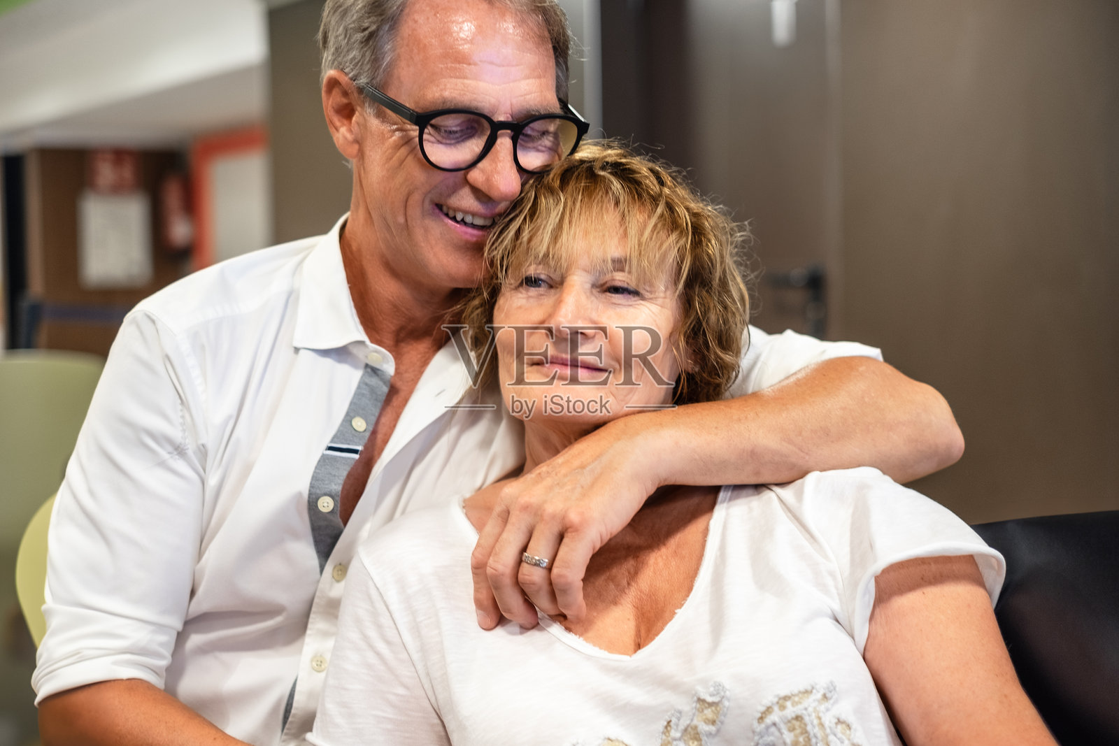 穿着白衬衫的帅气老年男子温柔地拥抱着他的妻子,表达着爱与关怀。成熟的夫妻坐在咖啡馆里互相依偎。照片摄影图片