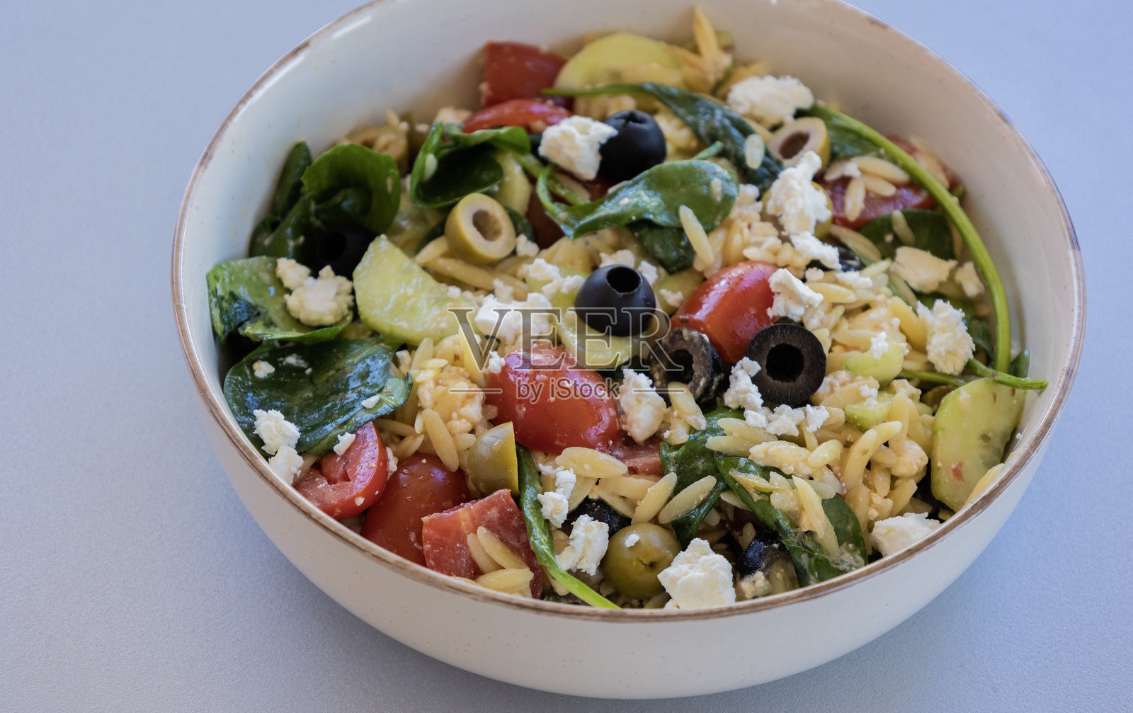 新鲜蔬菜、黑橄榄和碎羊奶酪制成的健康意大利米沙拉,盛在碗中,特写镜头。照片摄影图片