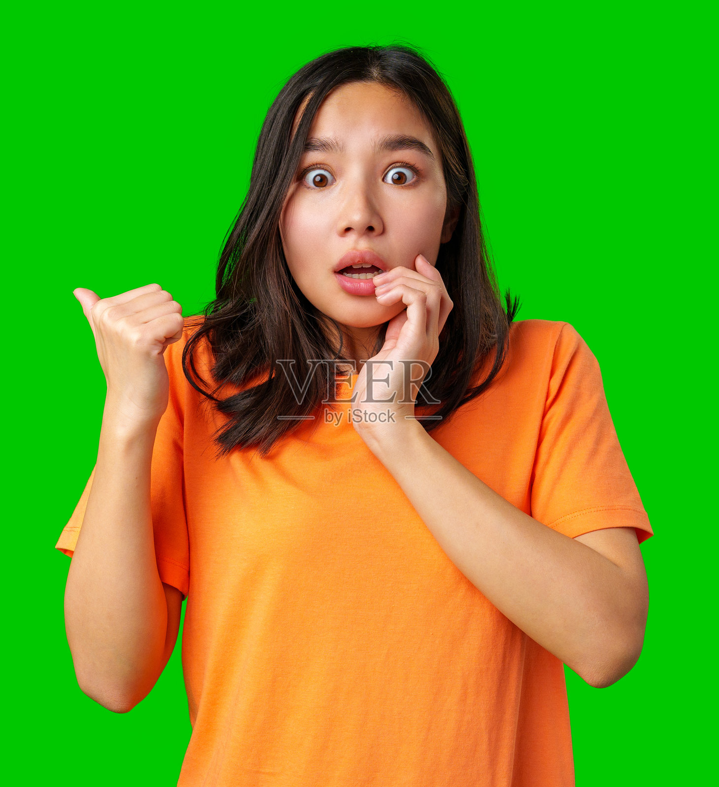 惊讶的女性用双手捂住脸,穿着明亮的橙色衬衫,背景为绿色。照片摄影图片