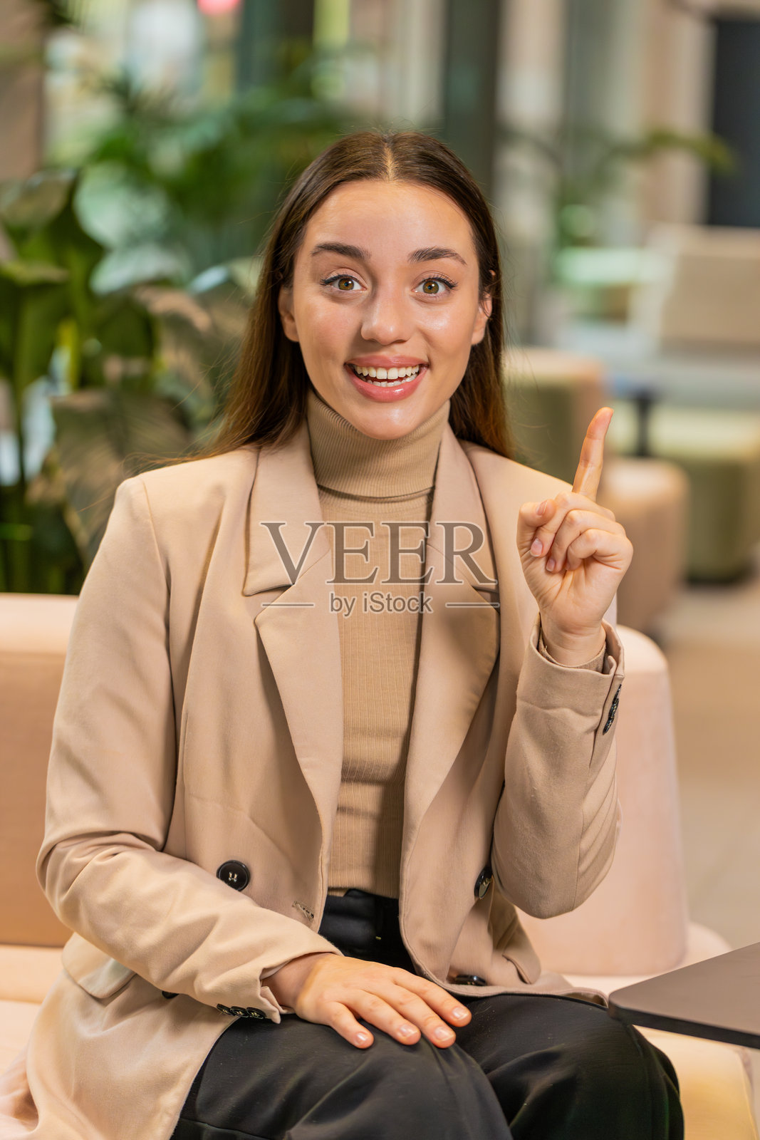 深思熟虑的聪明女性在办公室大堂中做手势,举起手指,想出了创意计划。照片摄影图片