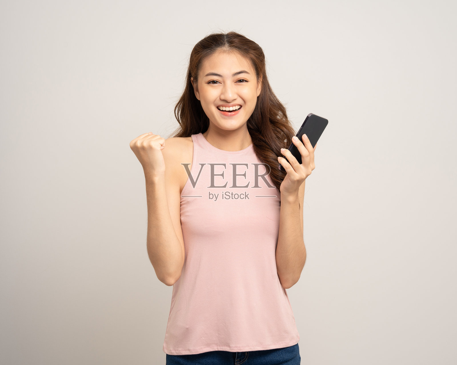 漂亮的年轻亚洲女性在孤立的白色背景上使用手机。快乐兴奋的年轻亚洲女性在手机上进行在线购物支付。正在智能手机上玩游戏。照片摄影图片