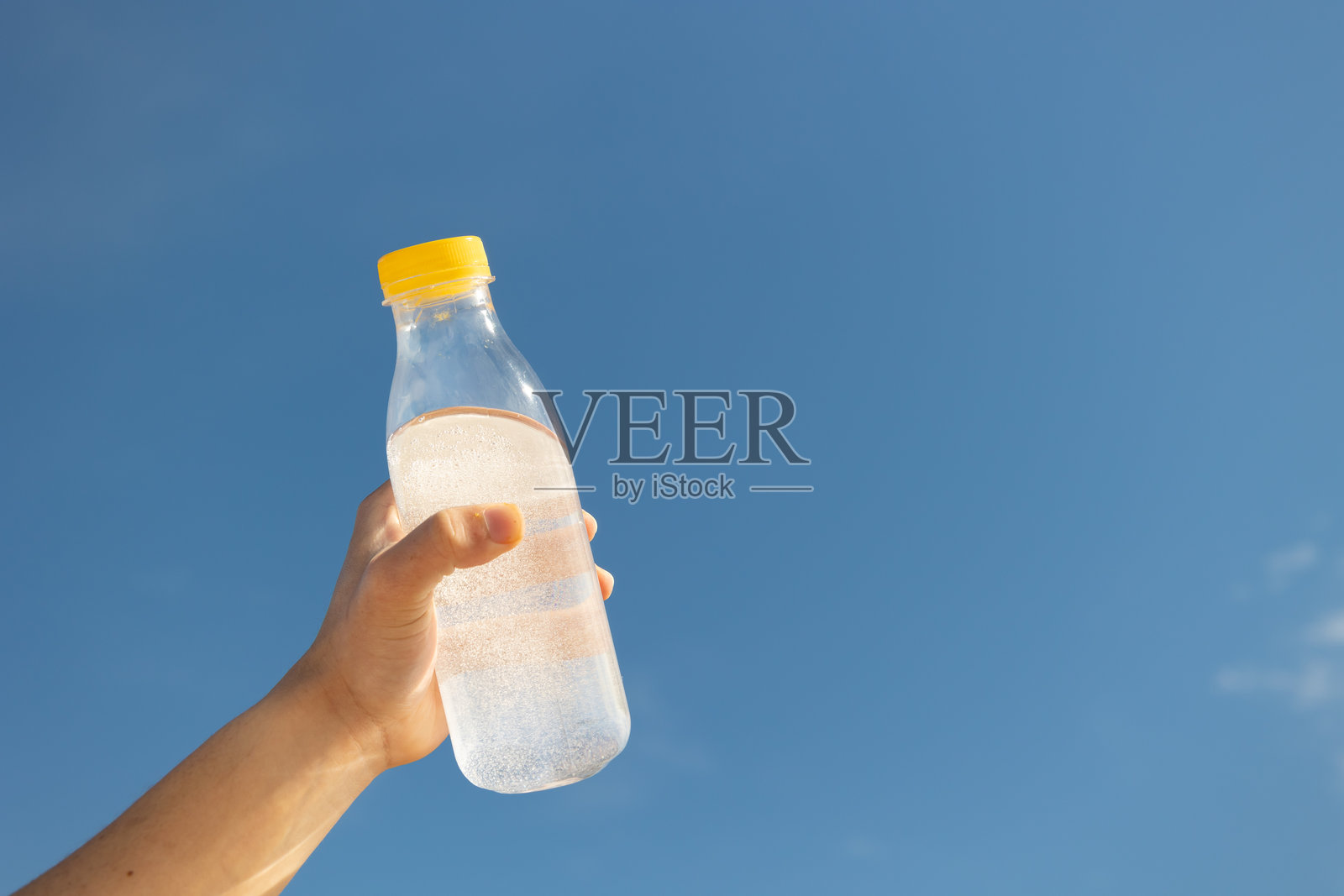 低角度拍摄的男性手握着一瓶清澈的水,背景是蓝天。照片摄影图片