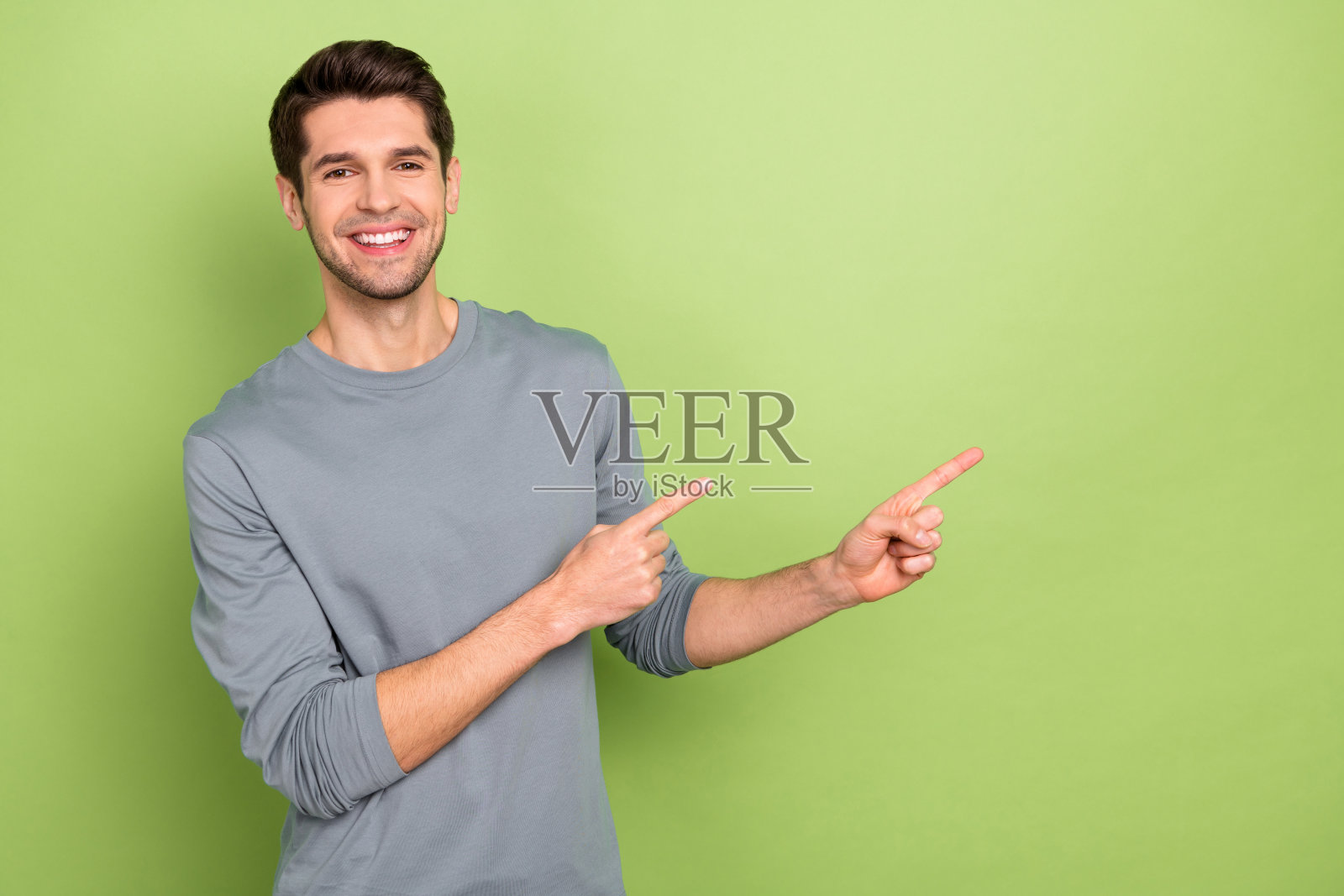 穿着灰色套头衫的酷炫年轻棕发男孩,背景为绿色。照片摄影图片