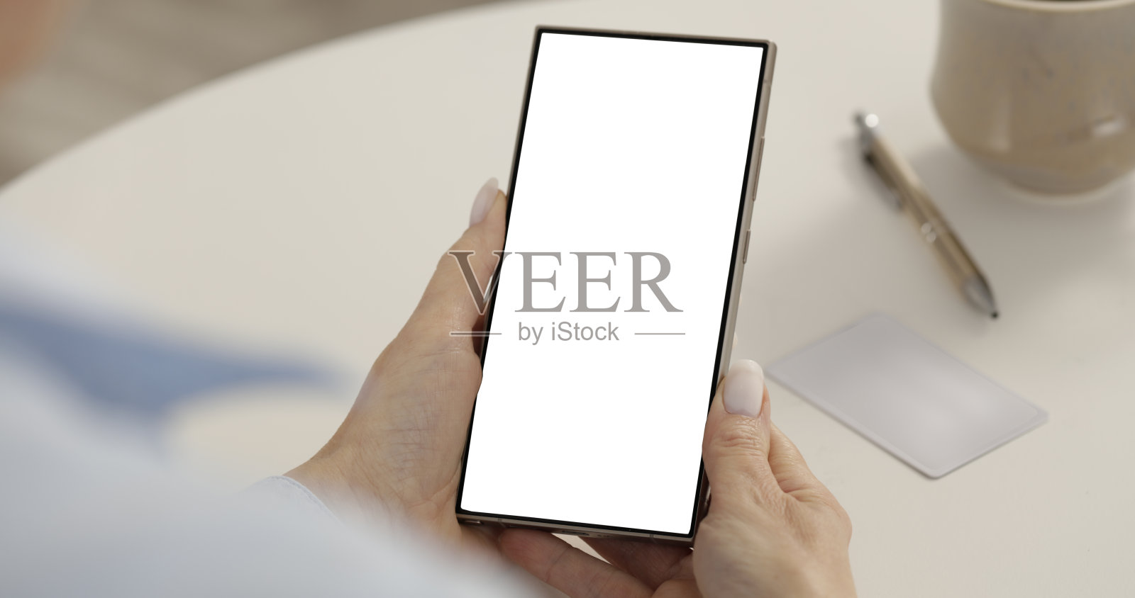 女性手部特写与白色桌面背景上的空白手机屏幕。空白显示屏,屏幕准备进行品牌推广。现代科技使用、在线活动和数字营销概念。照片摄影图片