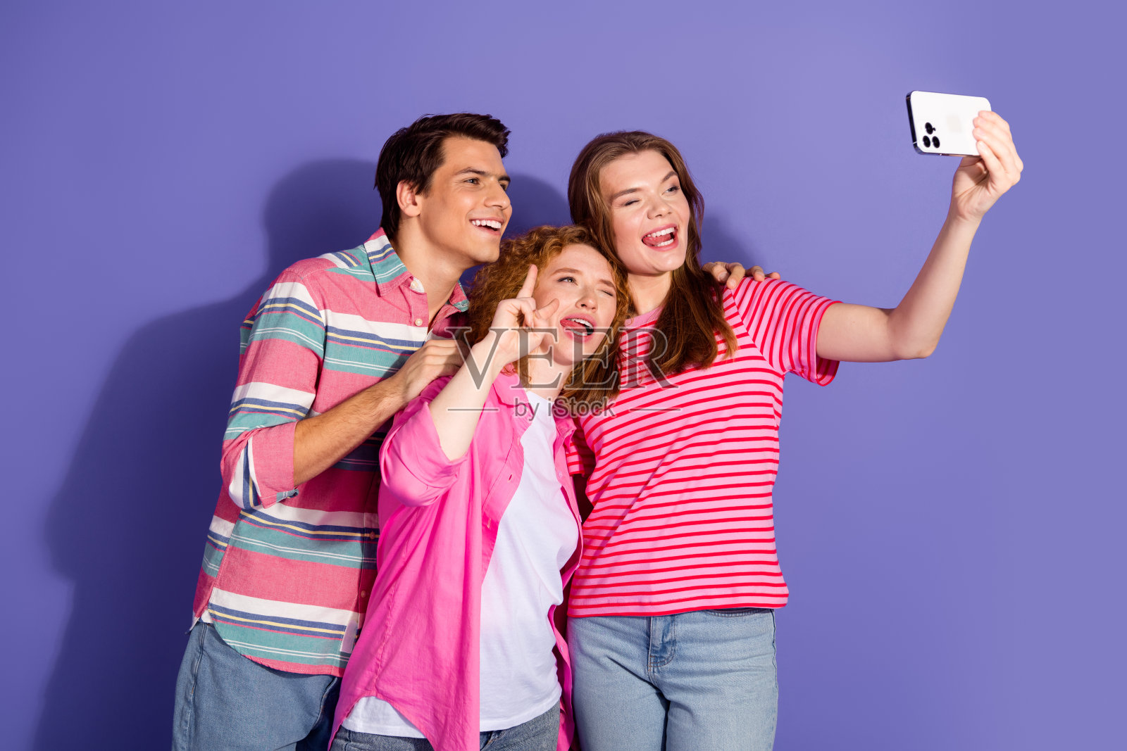 三位年轻朋友在紫色背景前自拍,穿着休闲服装,显得快乐而时尚。照片摄影图片
